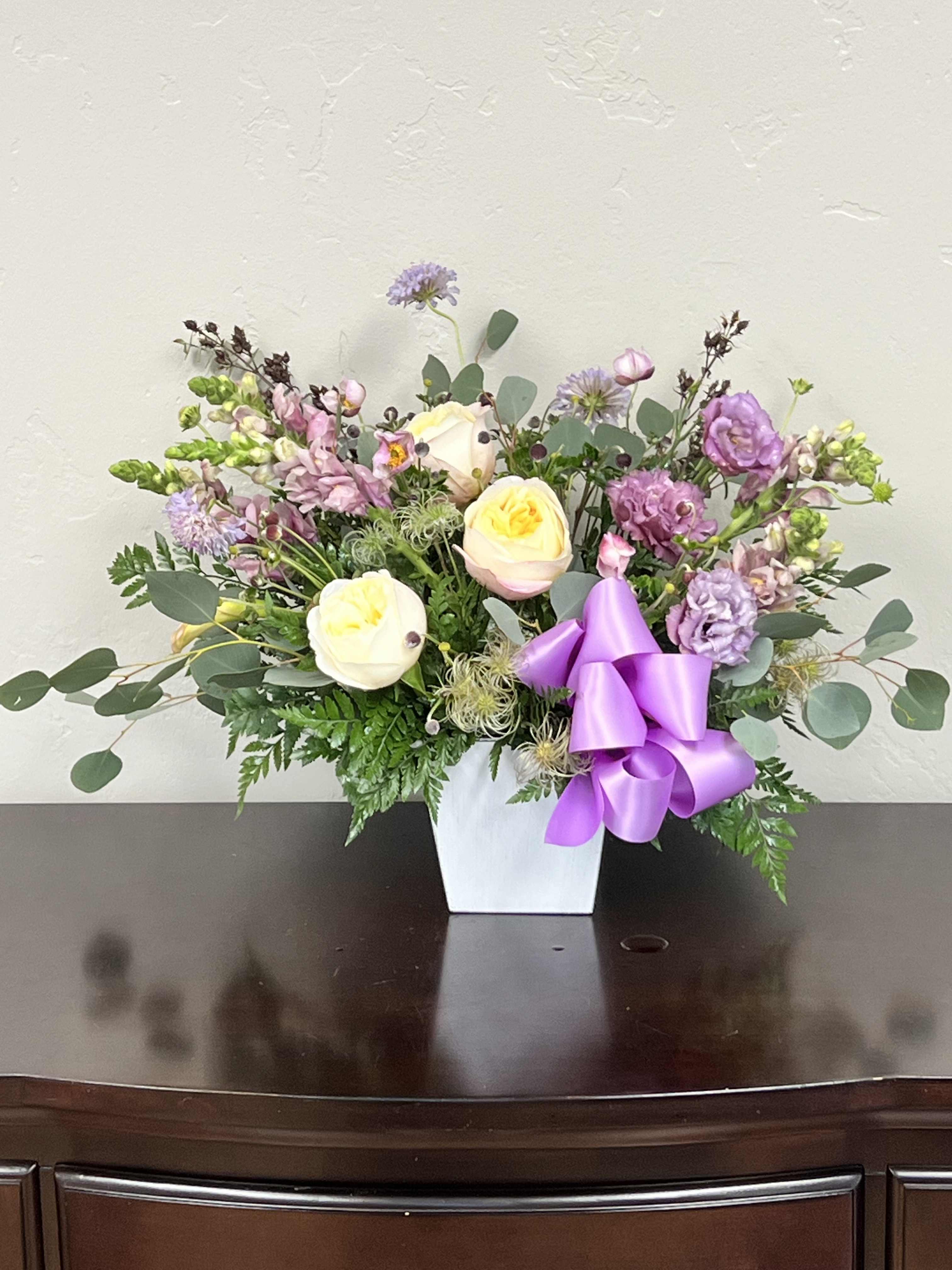 Pastel floral arrangement in a white vase with a purple ribbon