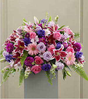 Farewell (DL) - We're heartbroken to hear about your loss and offer our deepest condolences. Our stunning funeral arrangement is the perfect way to honor your loved one and express your sincere sympathies. It's composed with an enchanting combination of stargazer lilies, purple roses, pink gerbera daisies, pink roses, purple lisianthus, pink stock, purple cushions, and luscious greenery, creating an elegant and memorable tribute.  