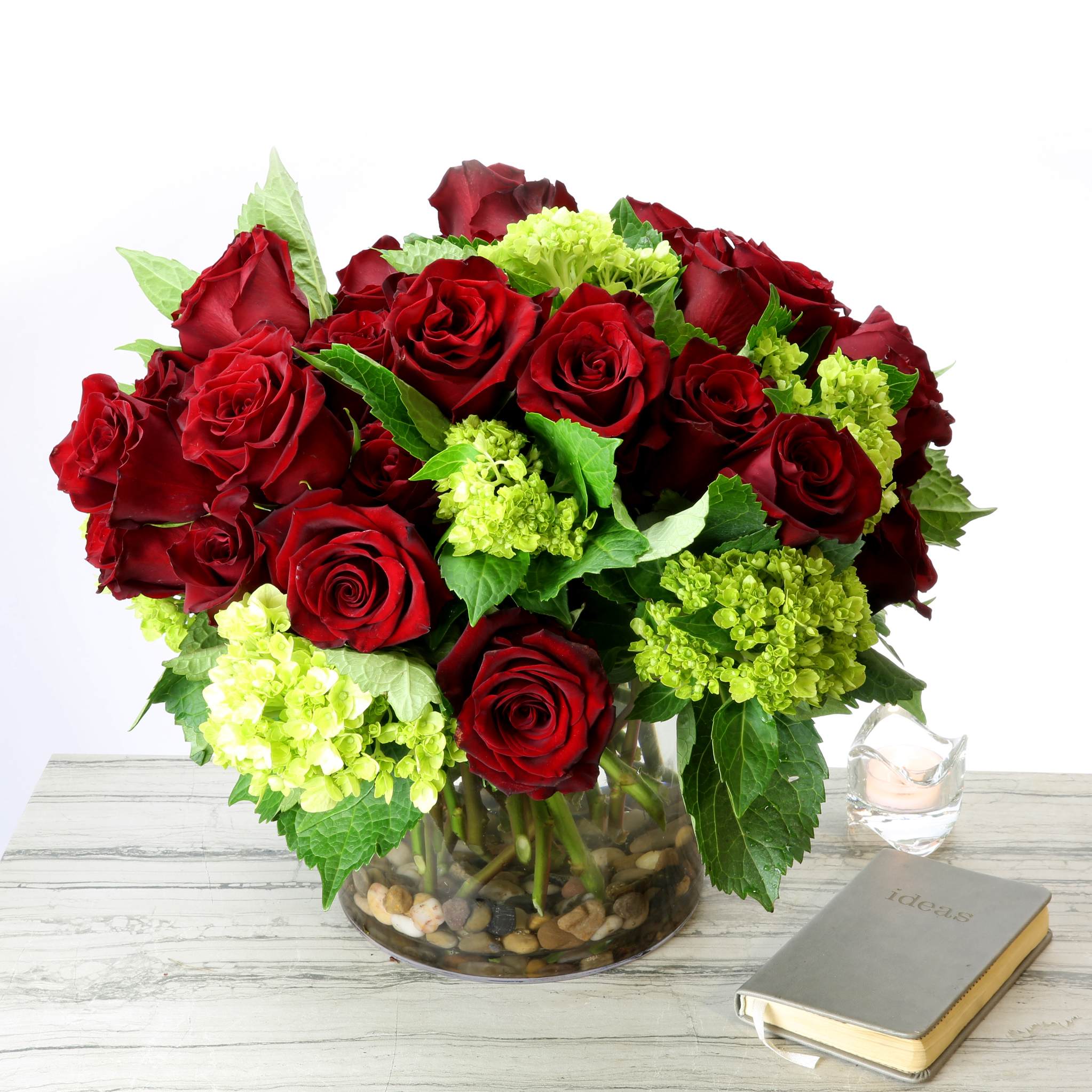 Red roses and green hydrangeas in a clear glass vase with pebbles