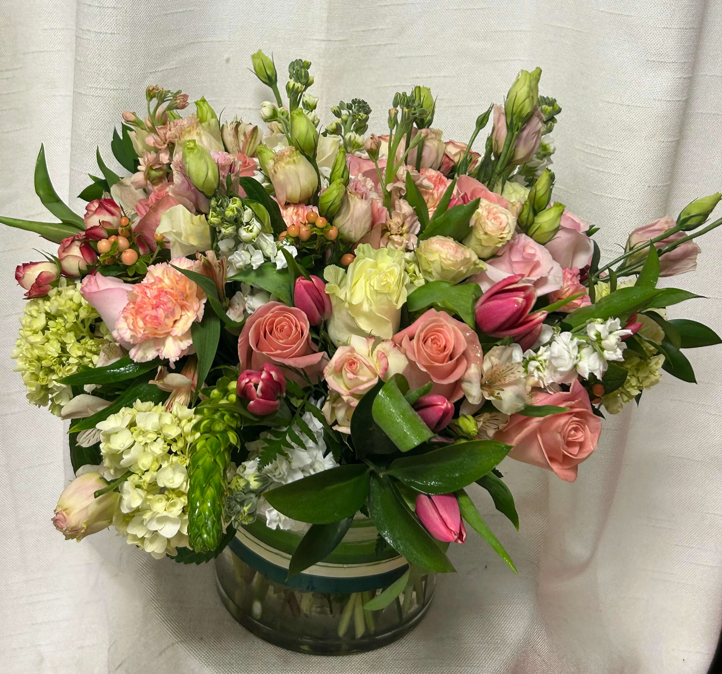 Motherly Love (DL) - This high-end floral composition combines delicate shades of light pink and white flowers, creating a vision of ethereal beauty and sophistication. Lisianthus, tulips, roses, stock, hypericum berries, hydrangea and assorted greens.