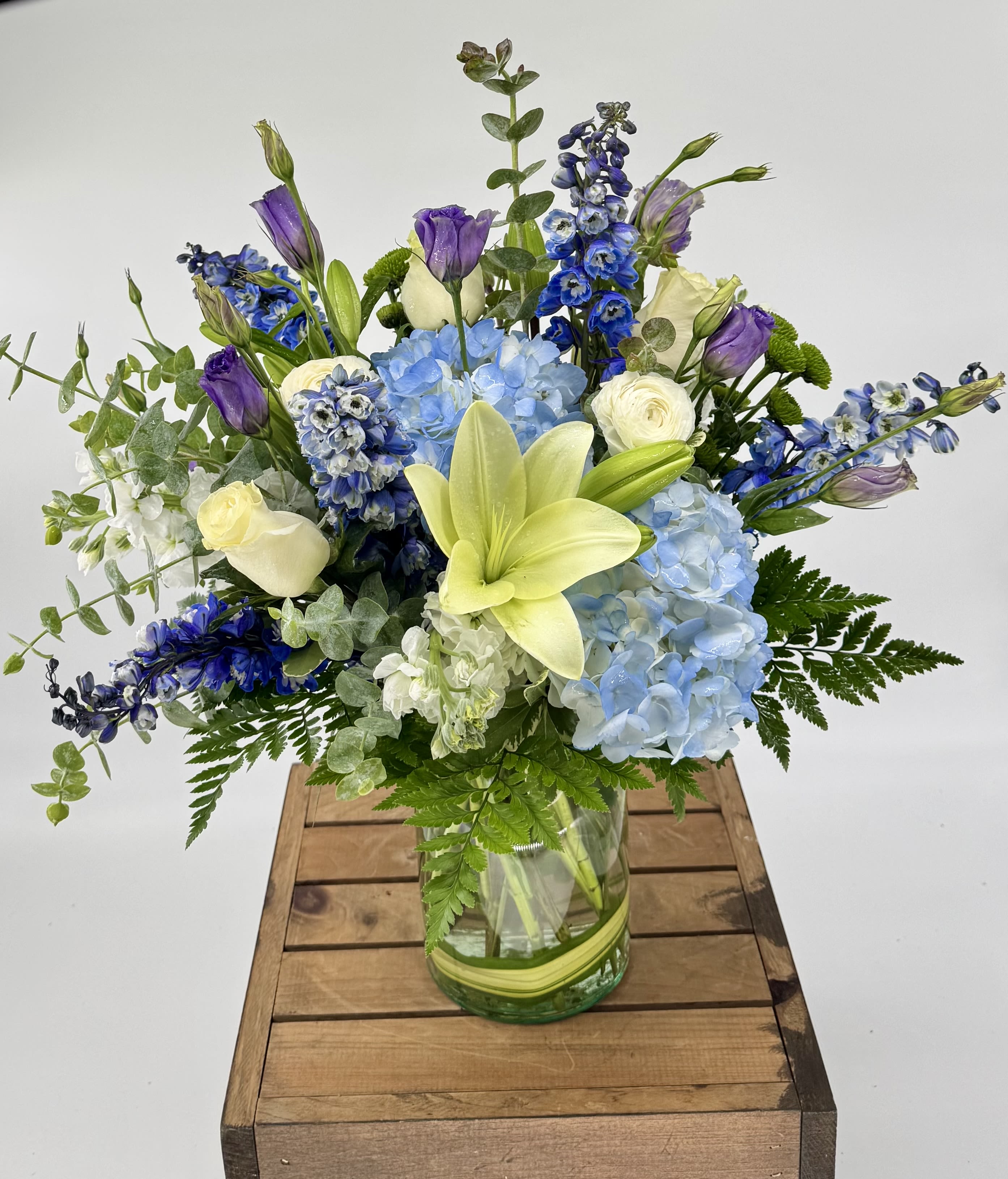 It's a Boy! (DL) - Celebrating the birth of your baby boy with blue Delphinium, purple Lisianthus, white Roses, and white Ranunculus—a perfect blend of strength, admiration, purity, and charm. This vibrant bouquet symbolizes love and new beginnings. 