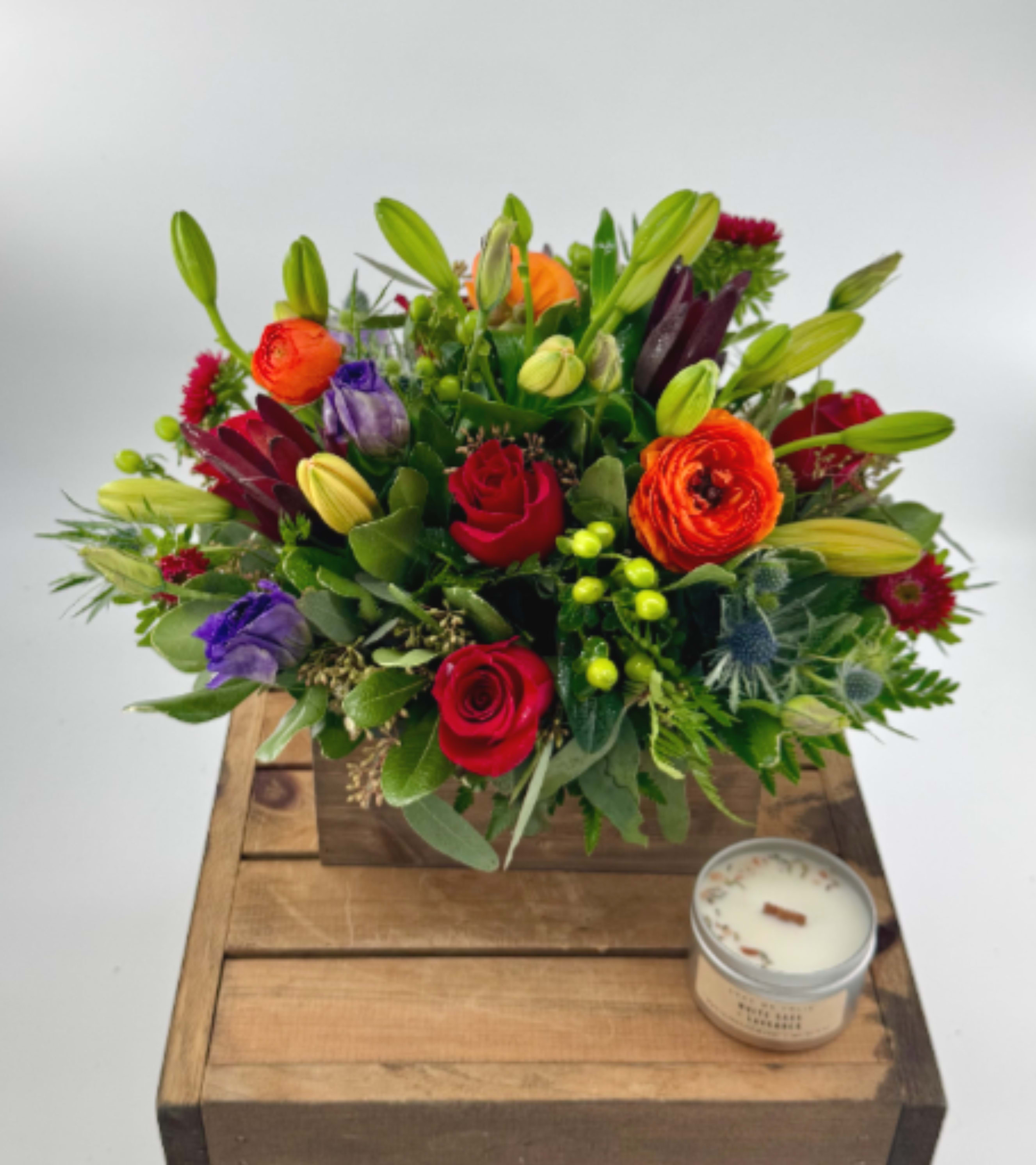 Colorful mixed flower arrangement in a wooden box with a candle beside it