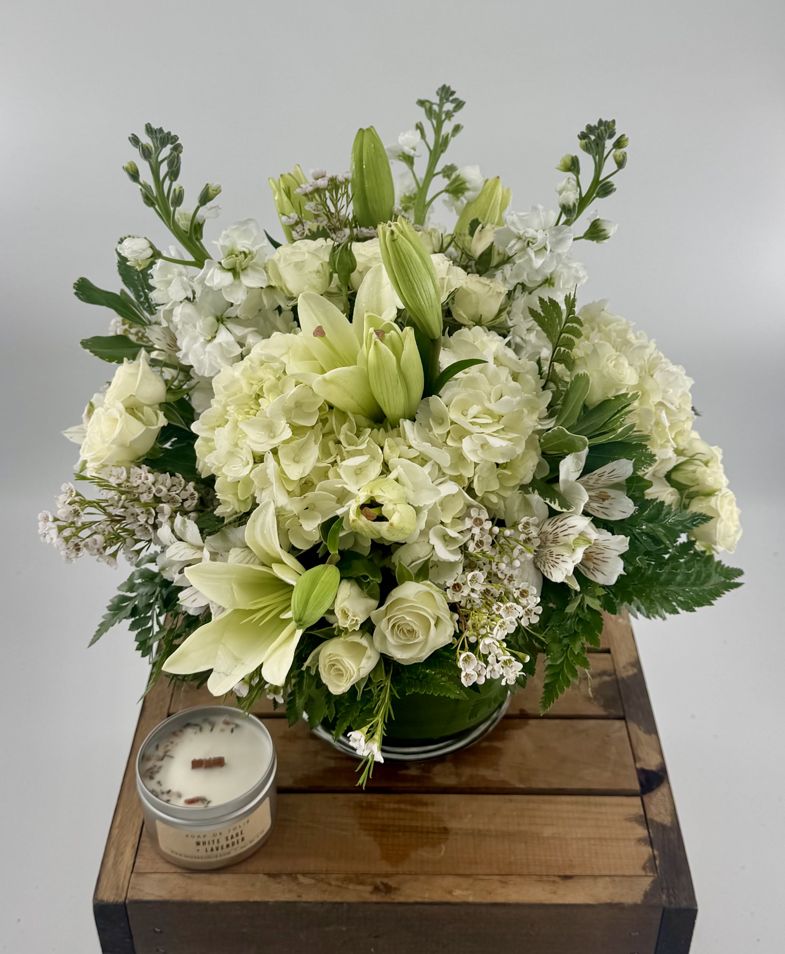 Moonlight (DL) - Experience timeless elegance with our modern all-white arrangement—featuring lush hydrangeas, spray roses, lilies, stock, and delicate wax flowers. Expertly crafted in a sleek 6x6" clear cylinder vase, it’s the perfect expression of grace and care for your most meaningful moments. 