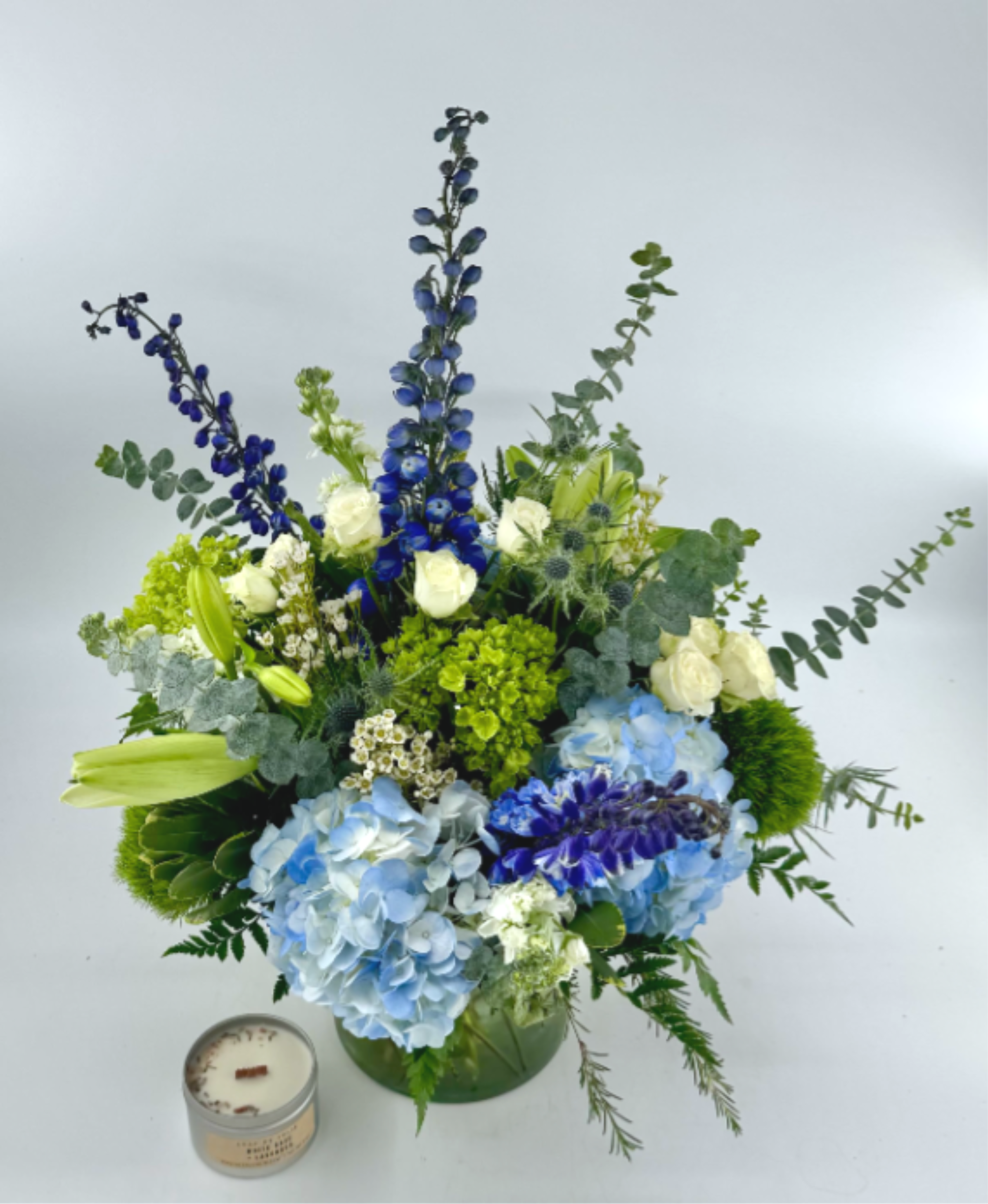 Blue and white floral arrangement in a green vase with a candle beside it
