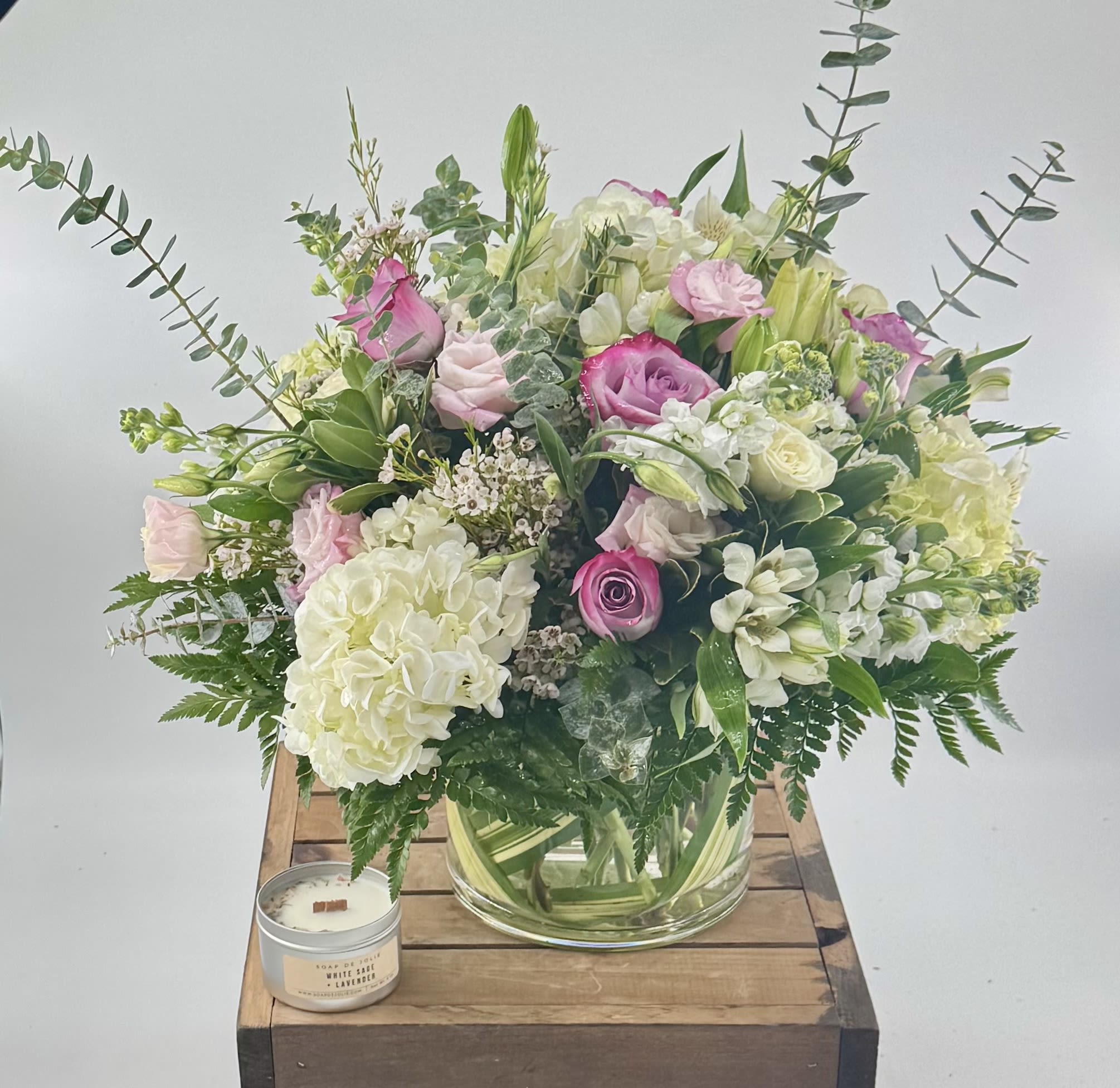 Paradise (DL) - Experience the perfect harmony of roses, hydrangea, white stock, and pink lisianthus, artfully enhanced with wax flower and eucalyptus. Elegantly arranged in a 7x7" glass cylinder vase, this modern design reflects our commitment to making your moments truly extraordinary. 