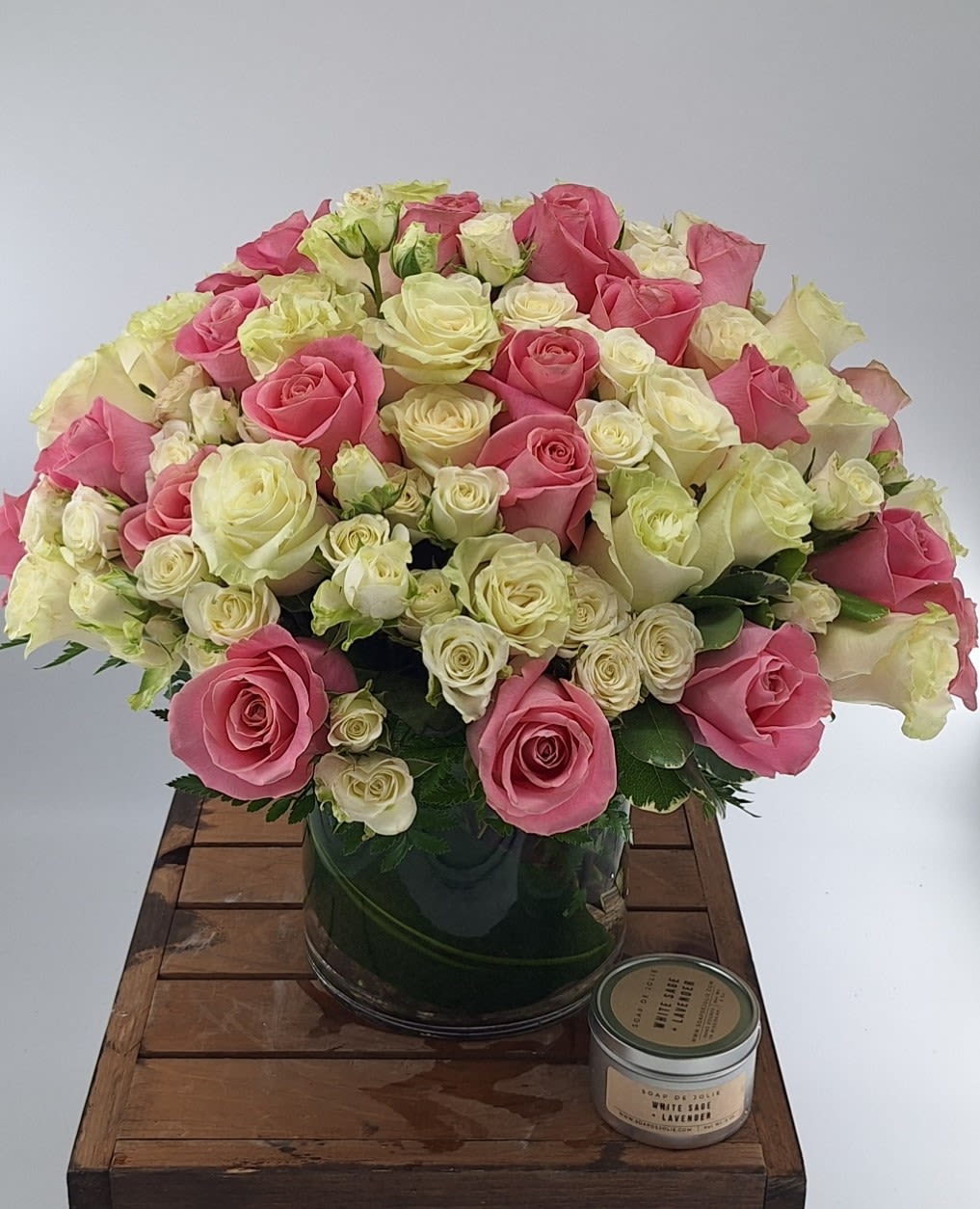 Pink and white roses arranged in a glass vase with a candle beside it