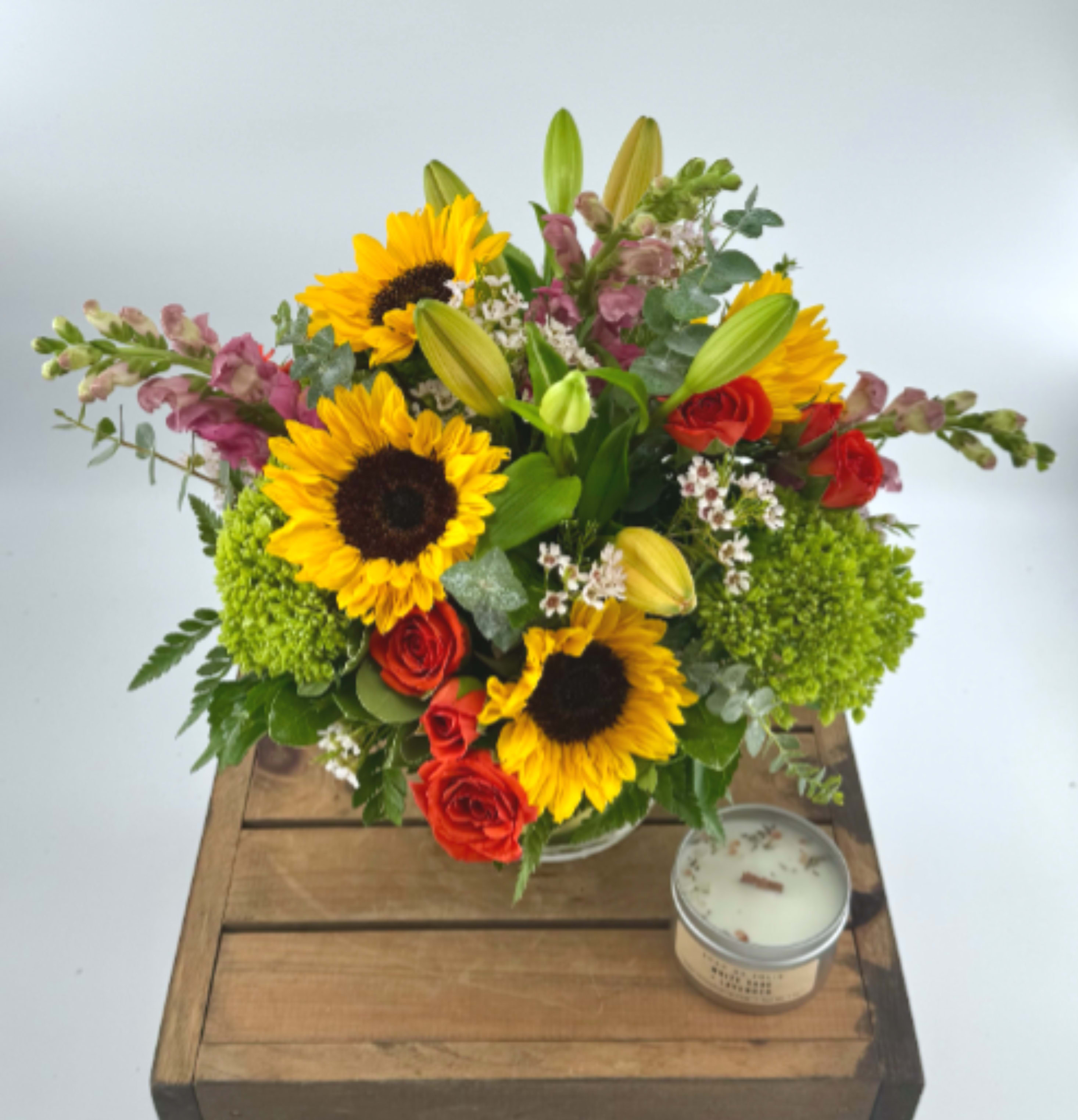 Citrus Splash  (DL) - Infuse your space with warmth and joy through this vibrant modern arrangement. Orange lilies, pink stock, sunflowers, green hydrangea, waxflower, and eucalyptus come together beautifully, expertly styled in a 5x5" glass cylinder vase—crafted to celebrate your moments with heartfelt elegance. 