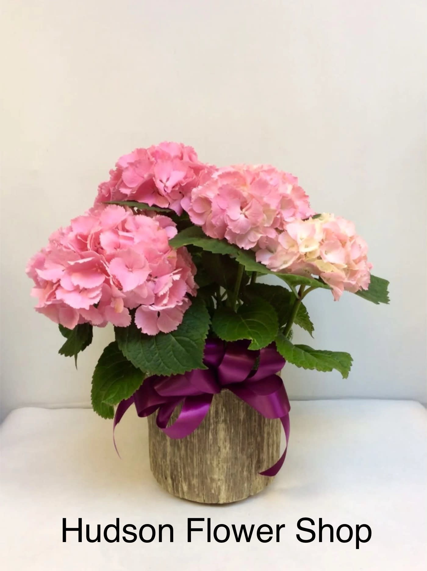 Pink hydrangeas in a rustic wooden container with a purple ribbon
