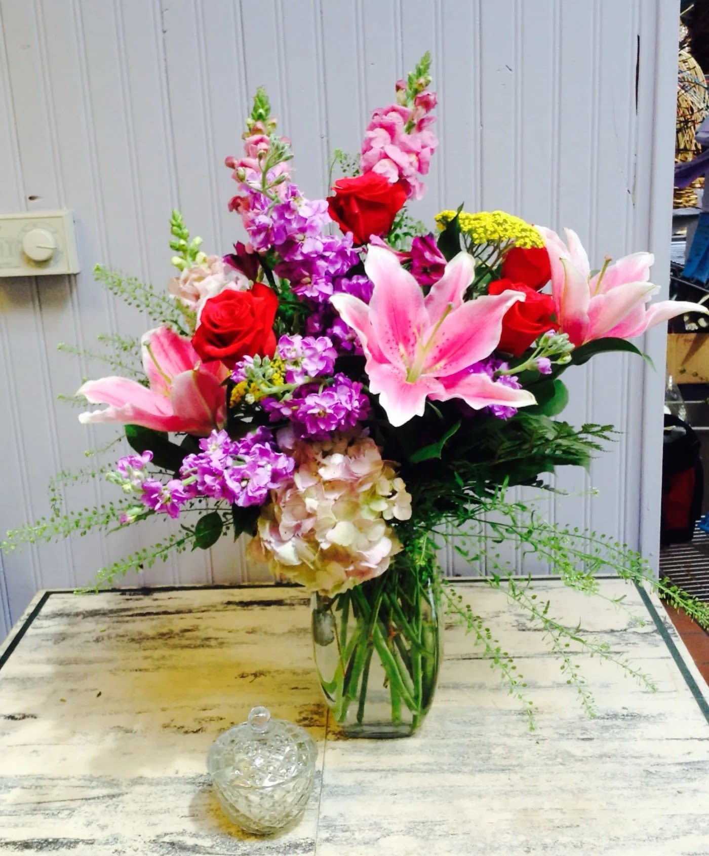Mixed bouquet of pink lilies, red roses, and purple flowers in a glass vase
