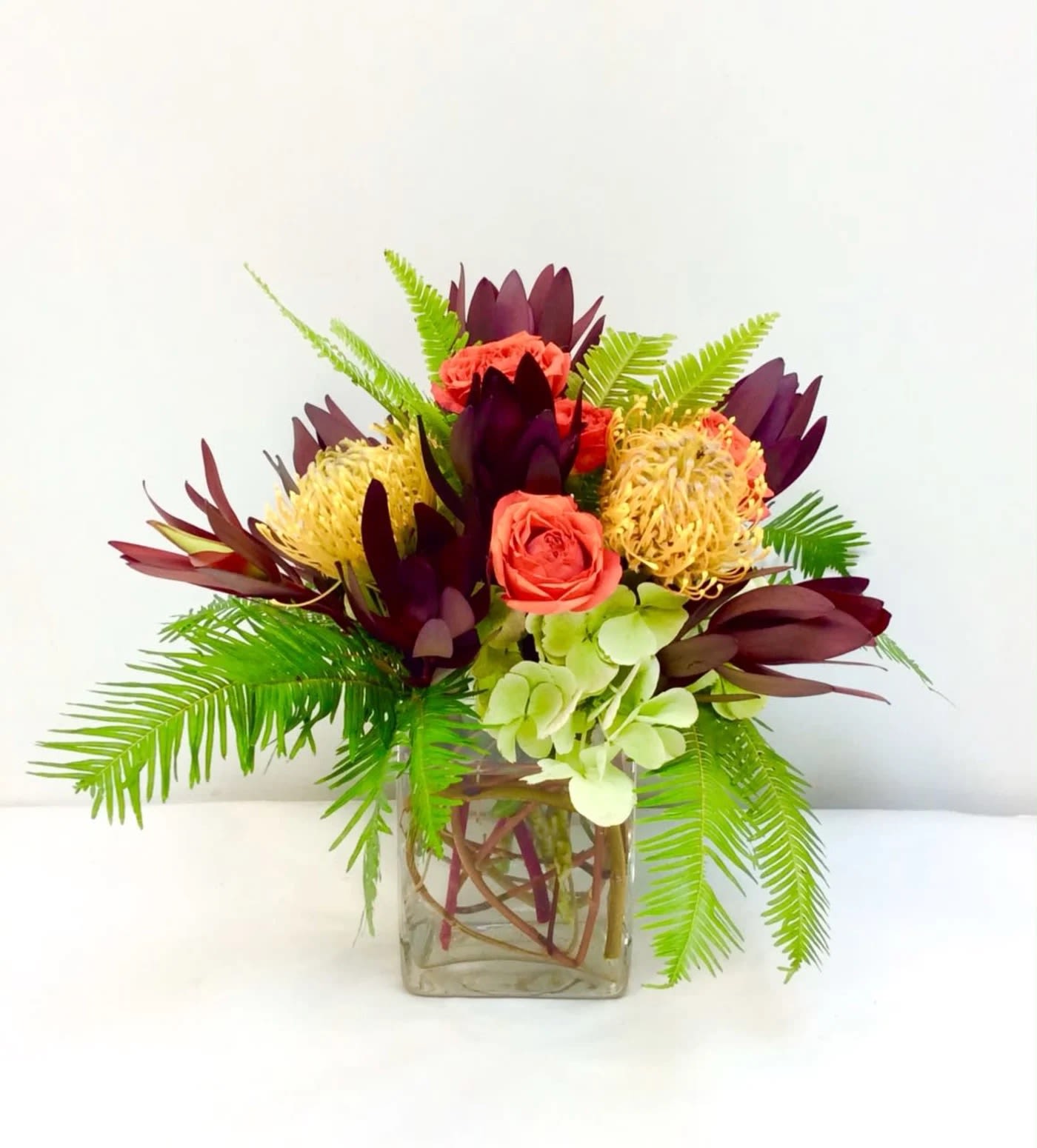 Tropical bouquet with coral roses and burgundy blooms in a square glass vase