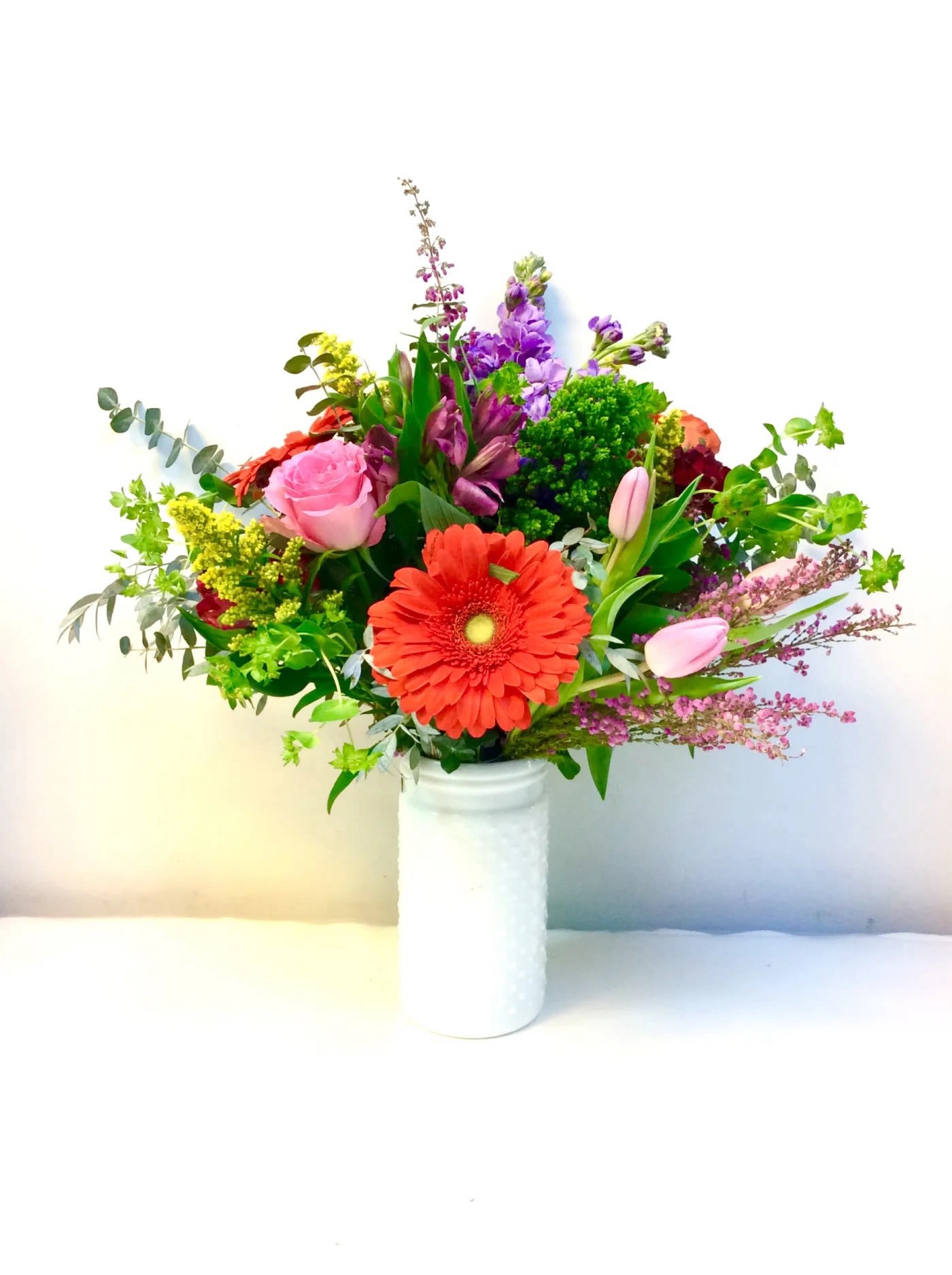 Mixed bouquet with a red gerbera daisy and pink roses in a white vase