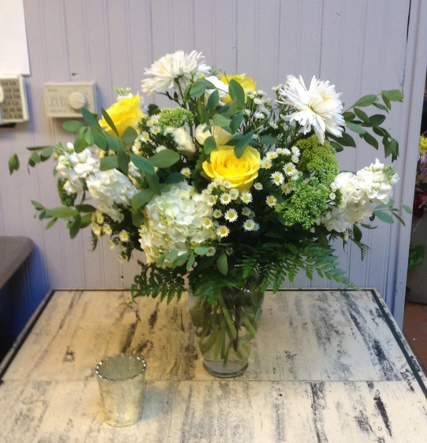 Yellow roses and white flowers arranged in a clear glass vase