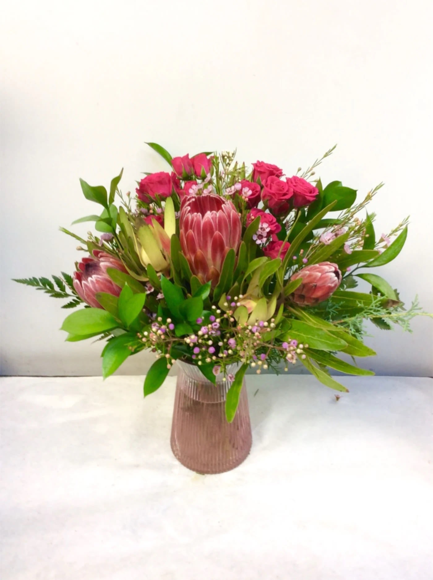Pink protea and roses arranged in a ribbed glass vase