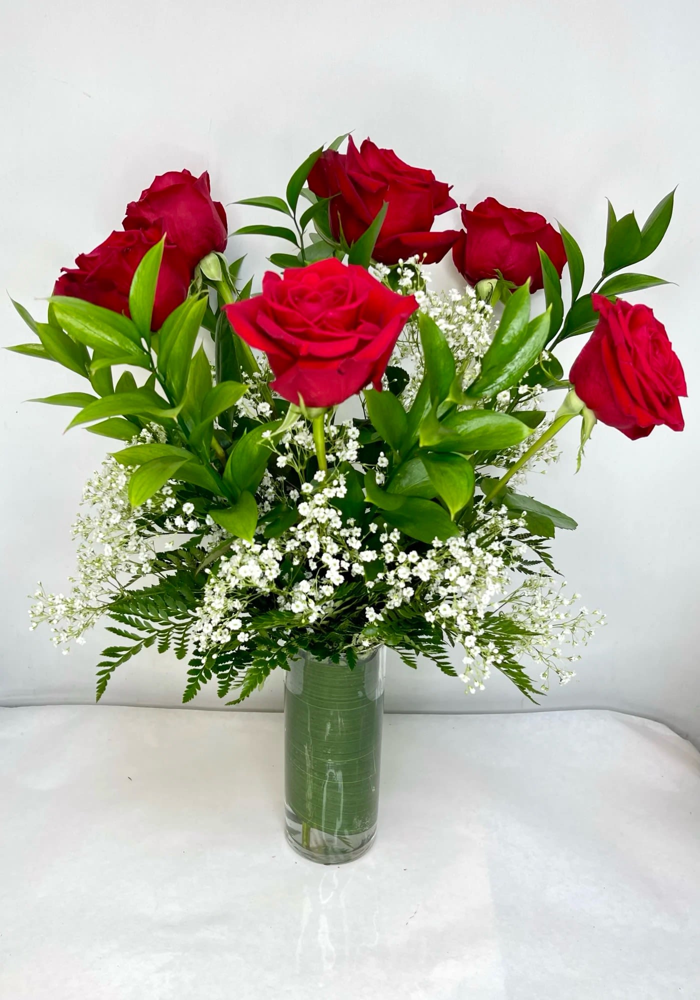 Red roses arranged in a clear glass vase with white filler flowers