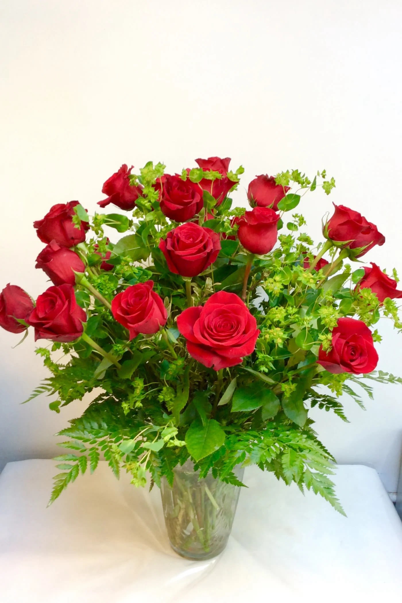 Red roses arranged in a clear glass vase with green filler
