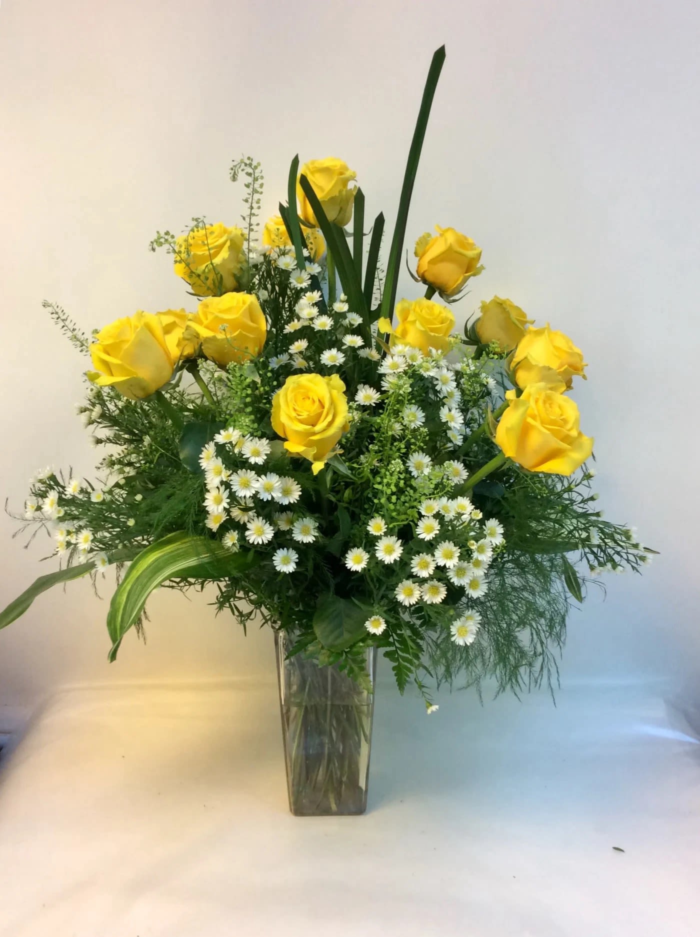 Yellow roses and white daisy flowers in a clear glass vase