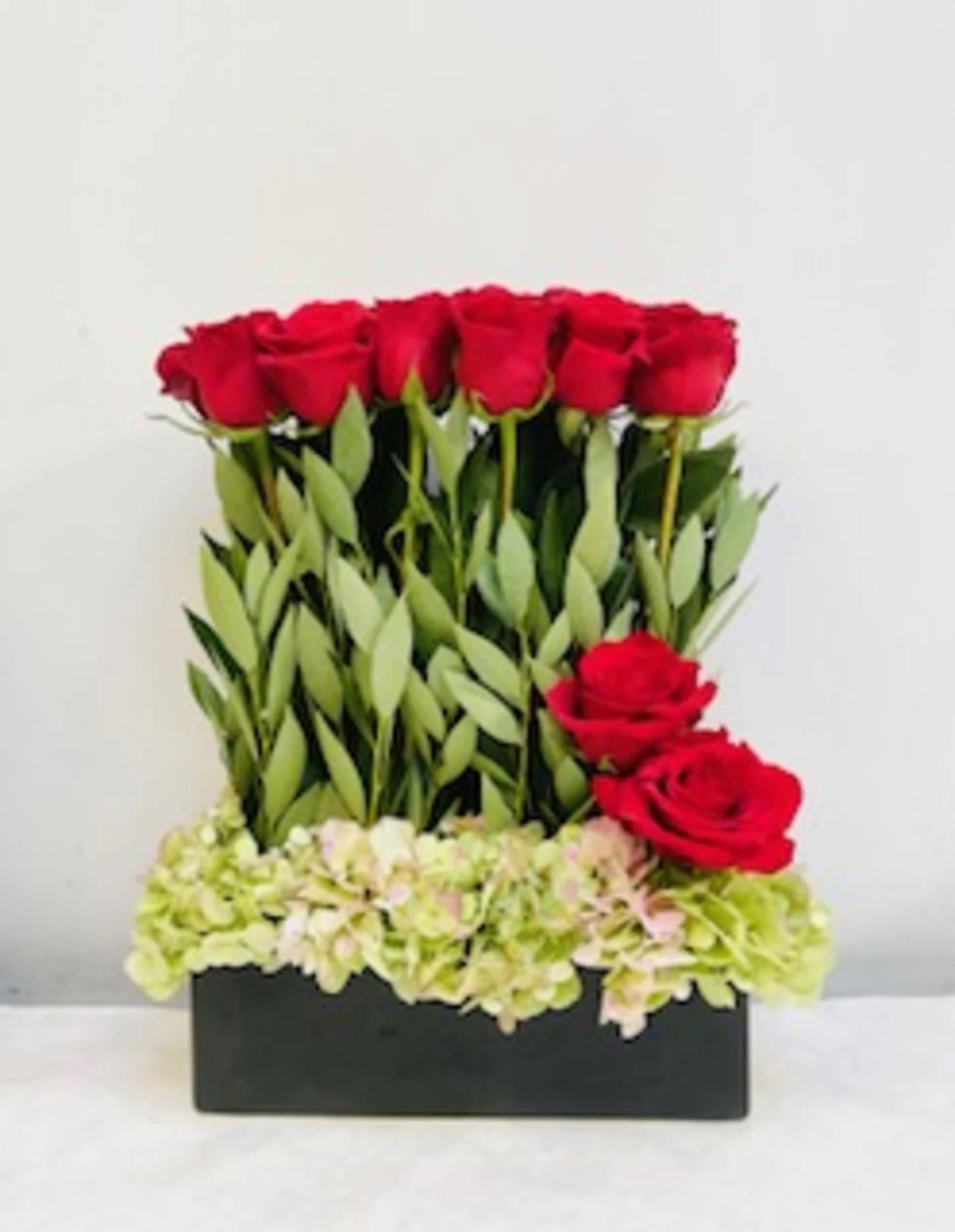 Red roses arranged in a black rectangular box with pale hydrangeas