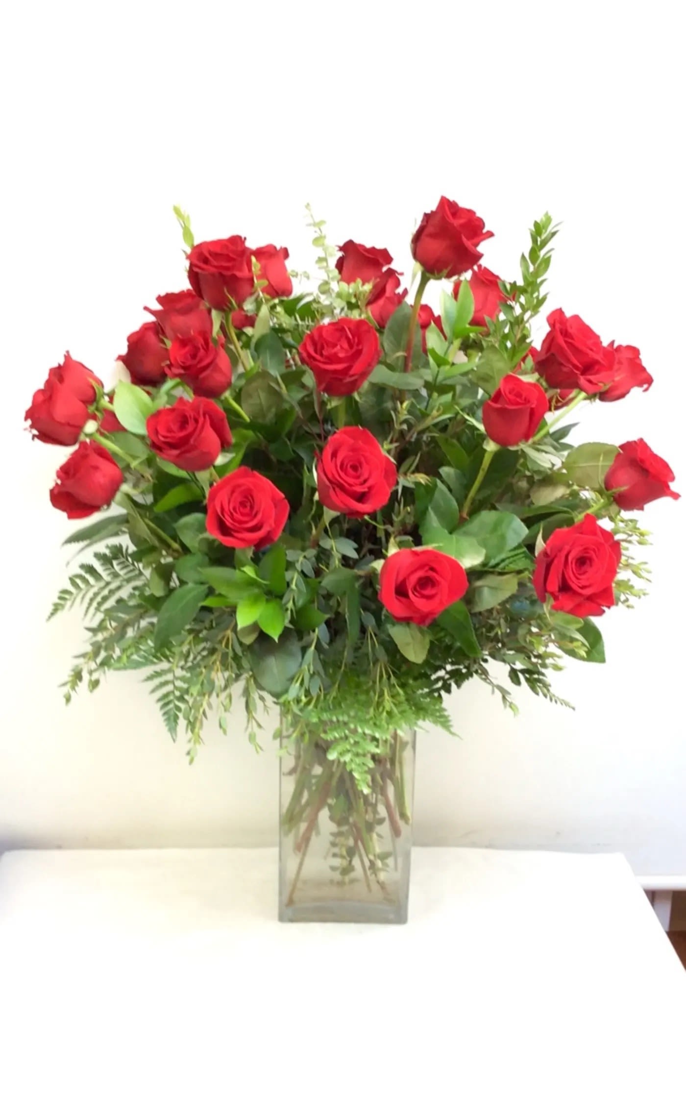 Red roses arranged in a clear glass vase with greenery