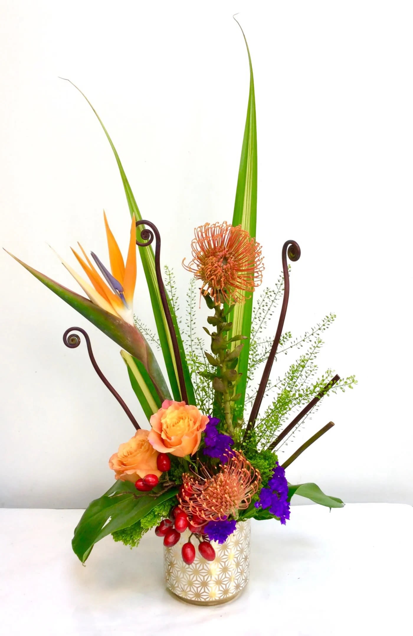 Tall tropical flower arrangement in a patterned vase with orange and purple blooms