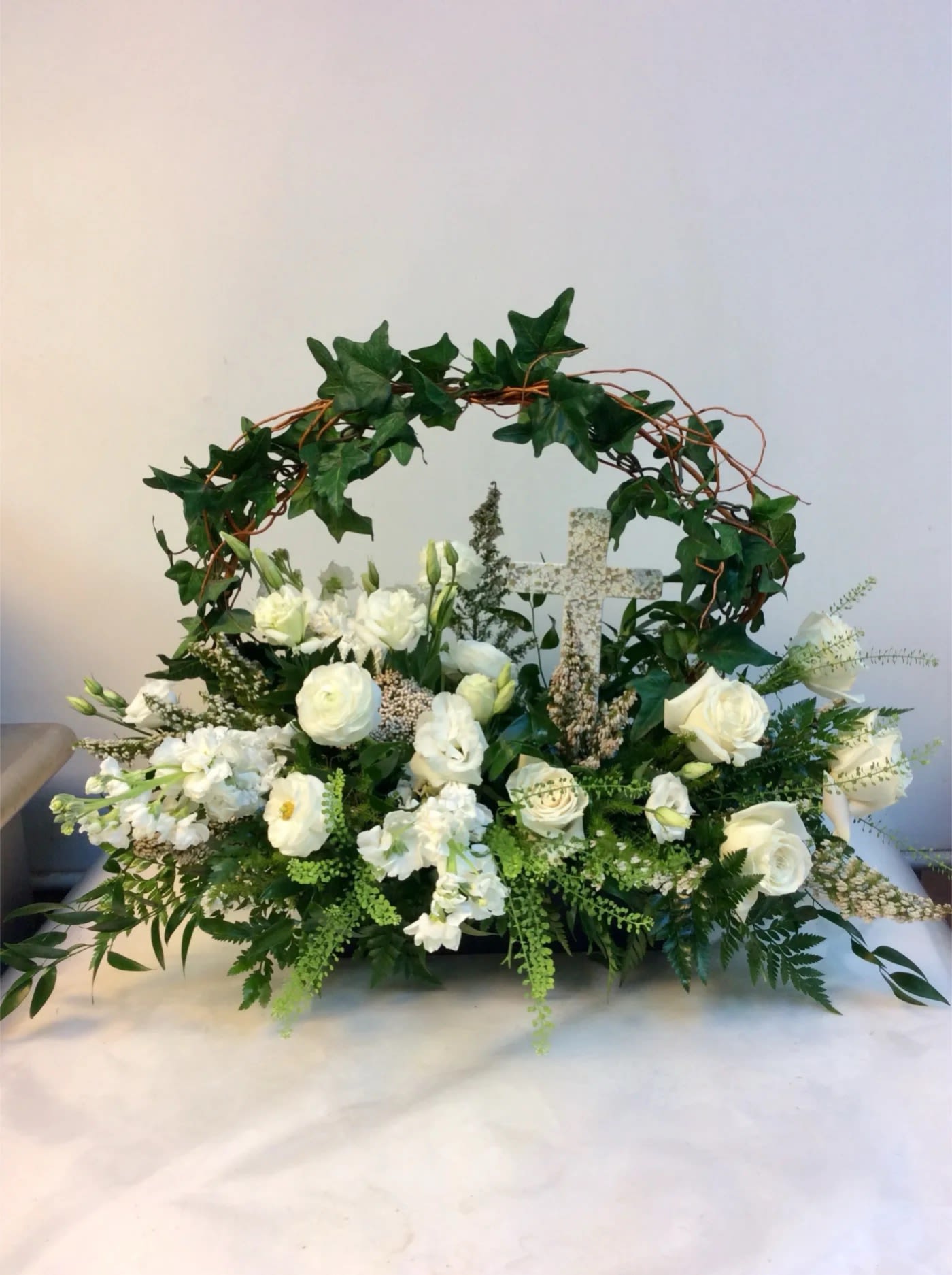 White floral arrangement with a decorative cross and ivy arch