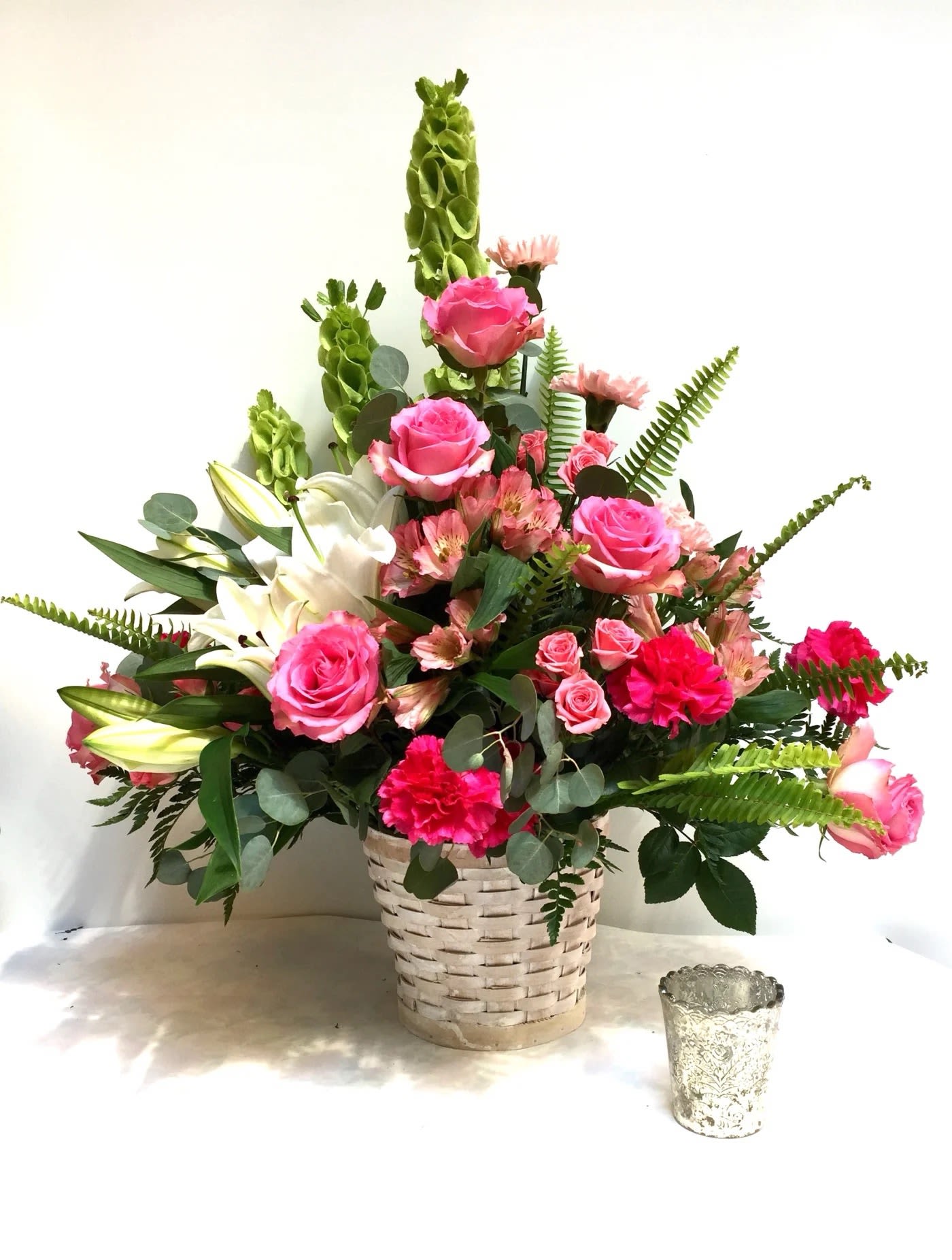 Pink roses and lilies arranged in a woven basket with greenery