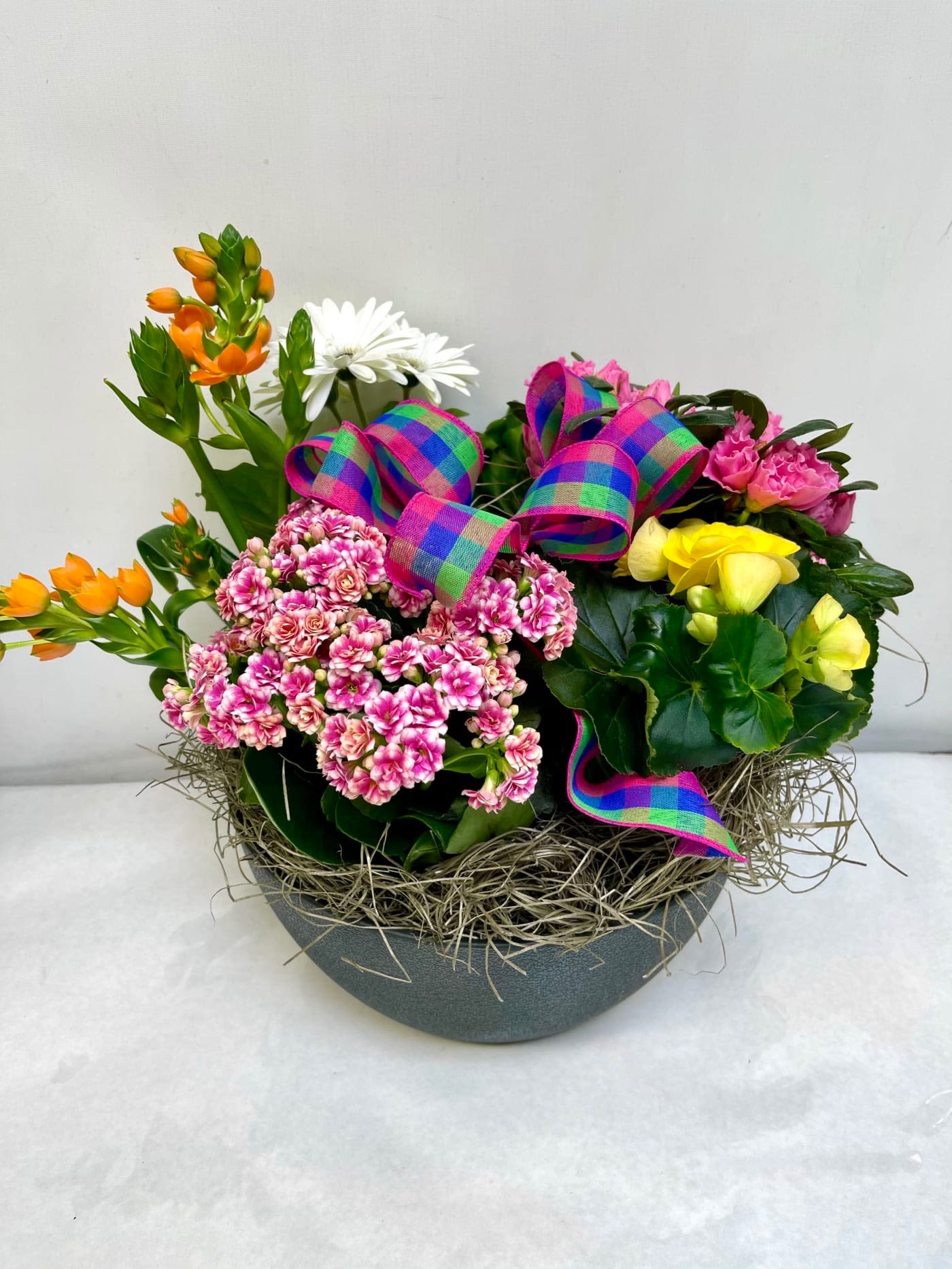 Mixed flower arrangement in a gray bowl with colorful ribbon bows