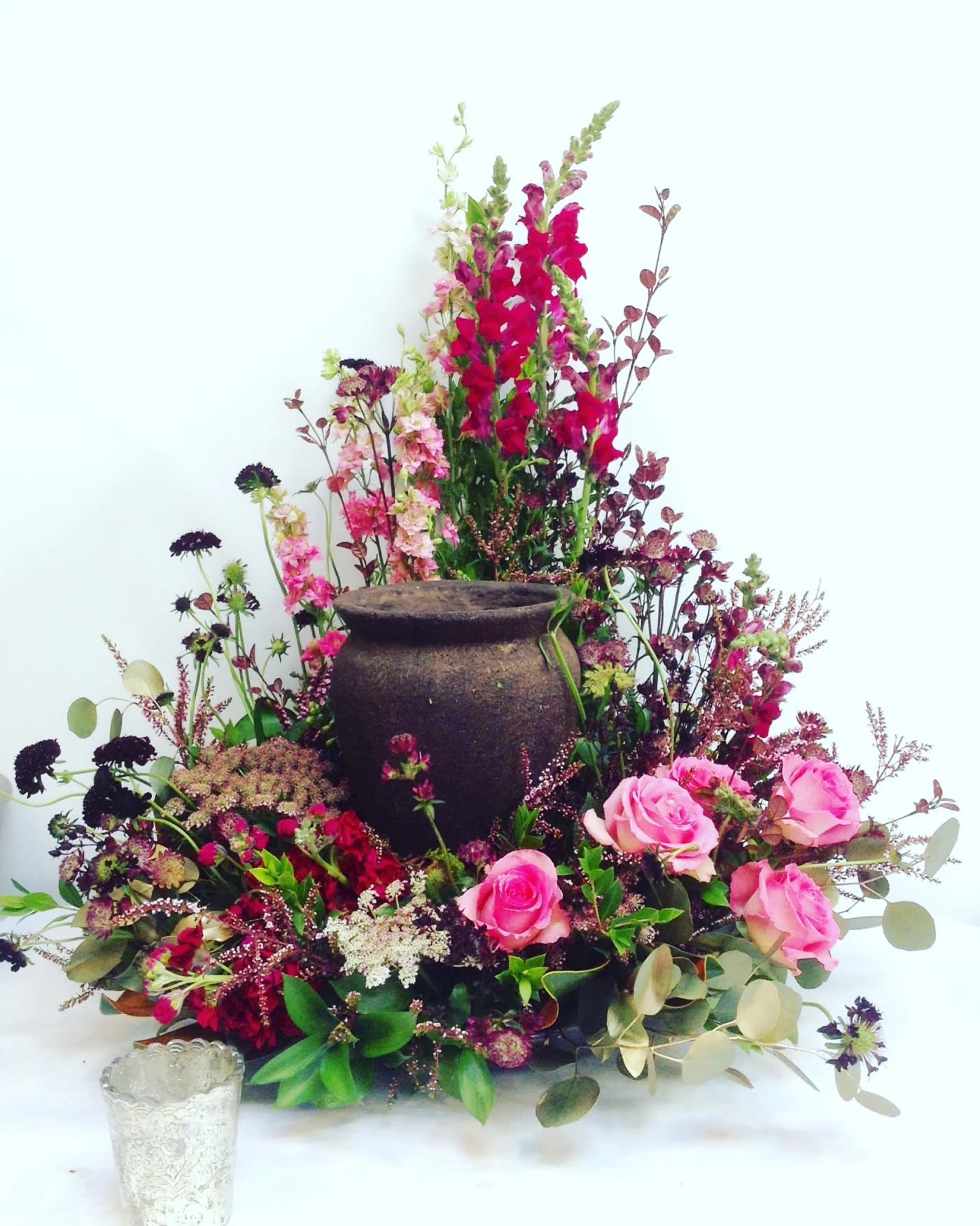 Pink roses and mixed flowers arranged around a dark urn centerpiece