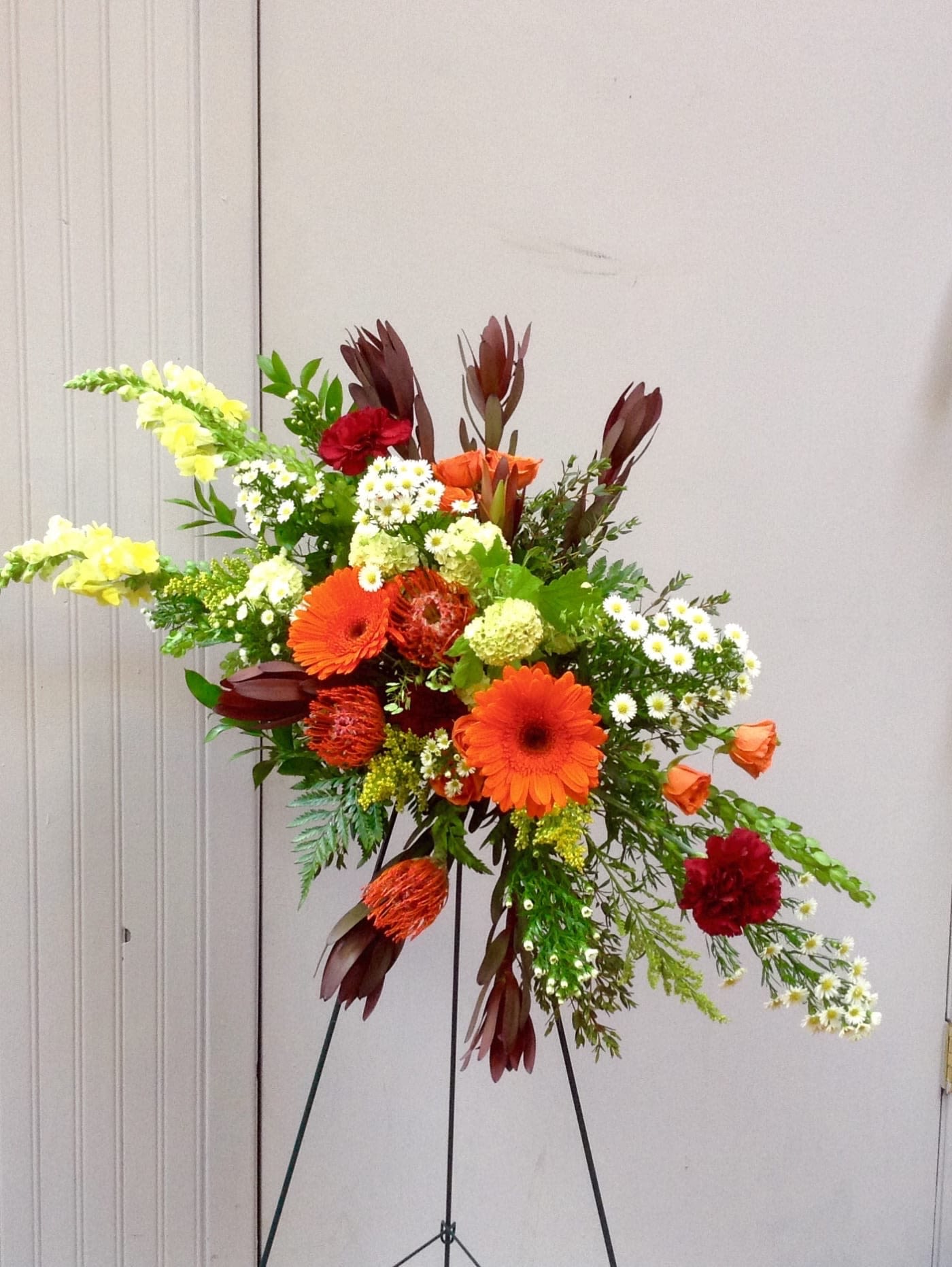 Tall mixed floral arrangement with orange gerberas and red blooms on a stand
