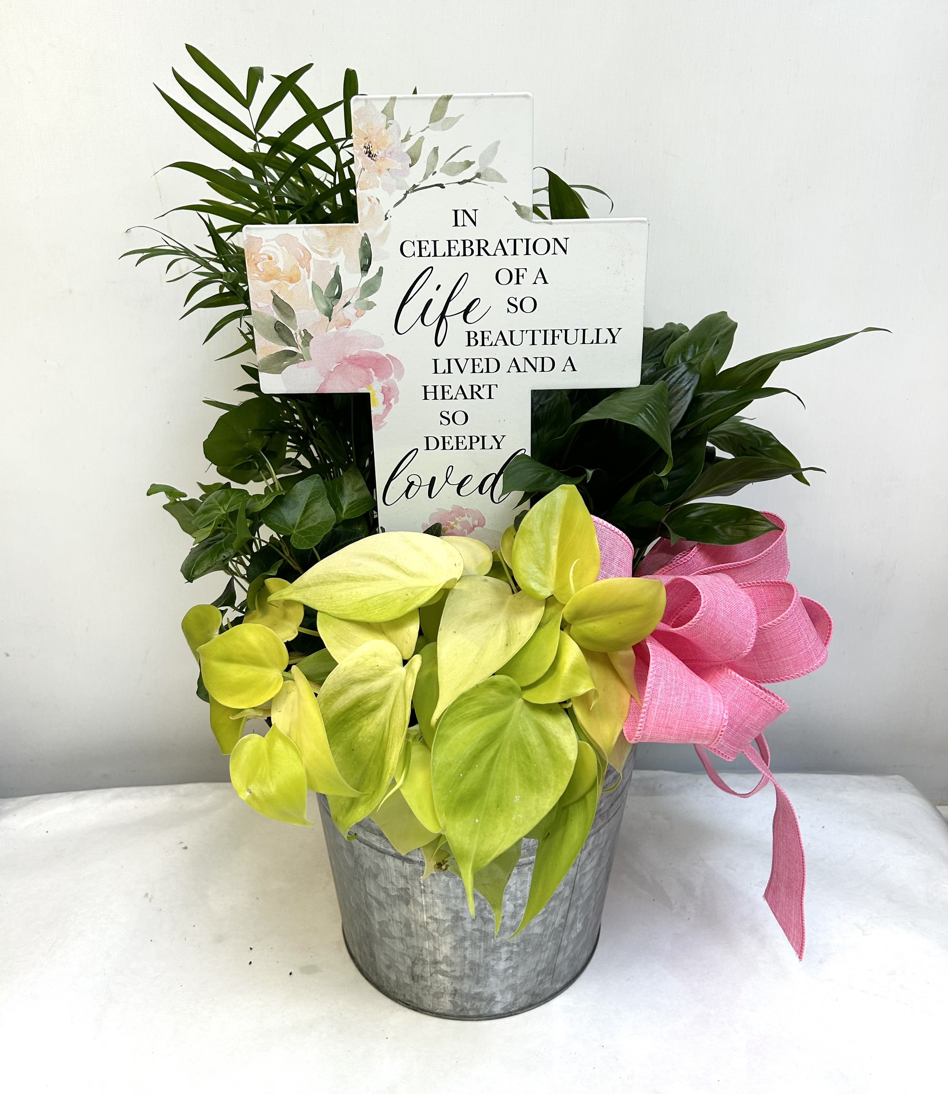 Potted plant arrangement with a memorial cross sign and pink ribbon