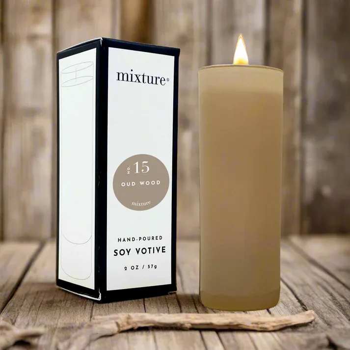 Lit beige soy votive candle beside its box