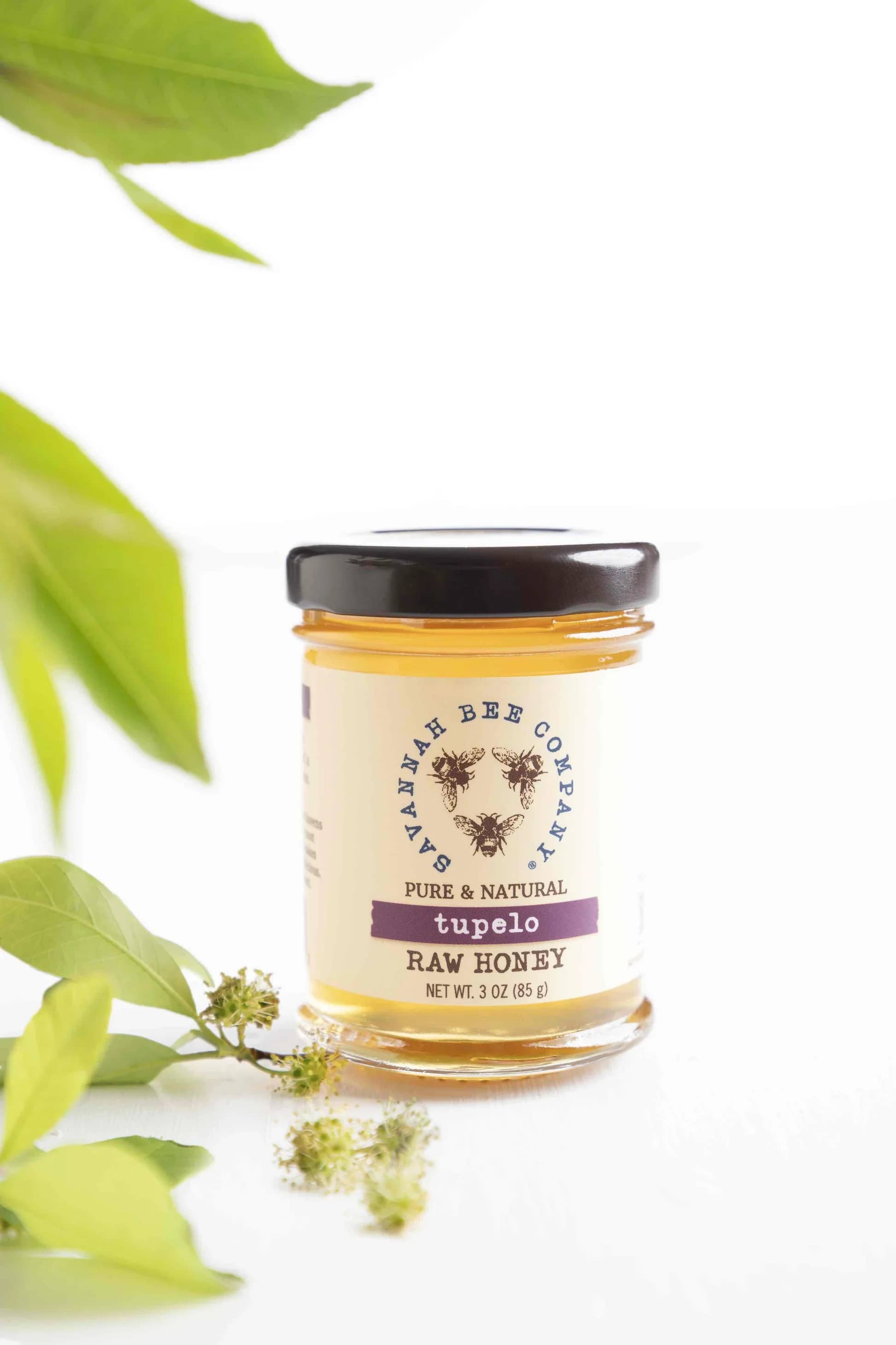 Jar of tupelo raw honey with green leaves beside it