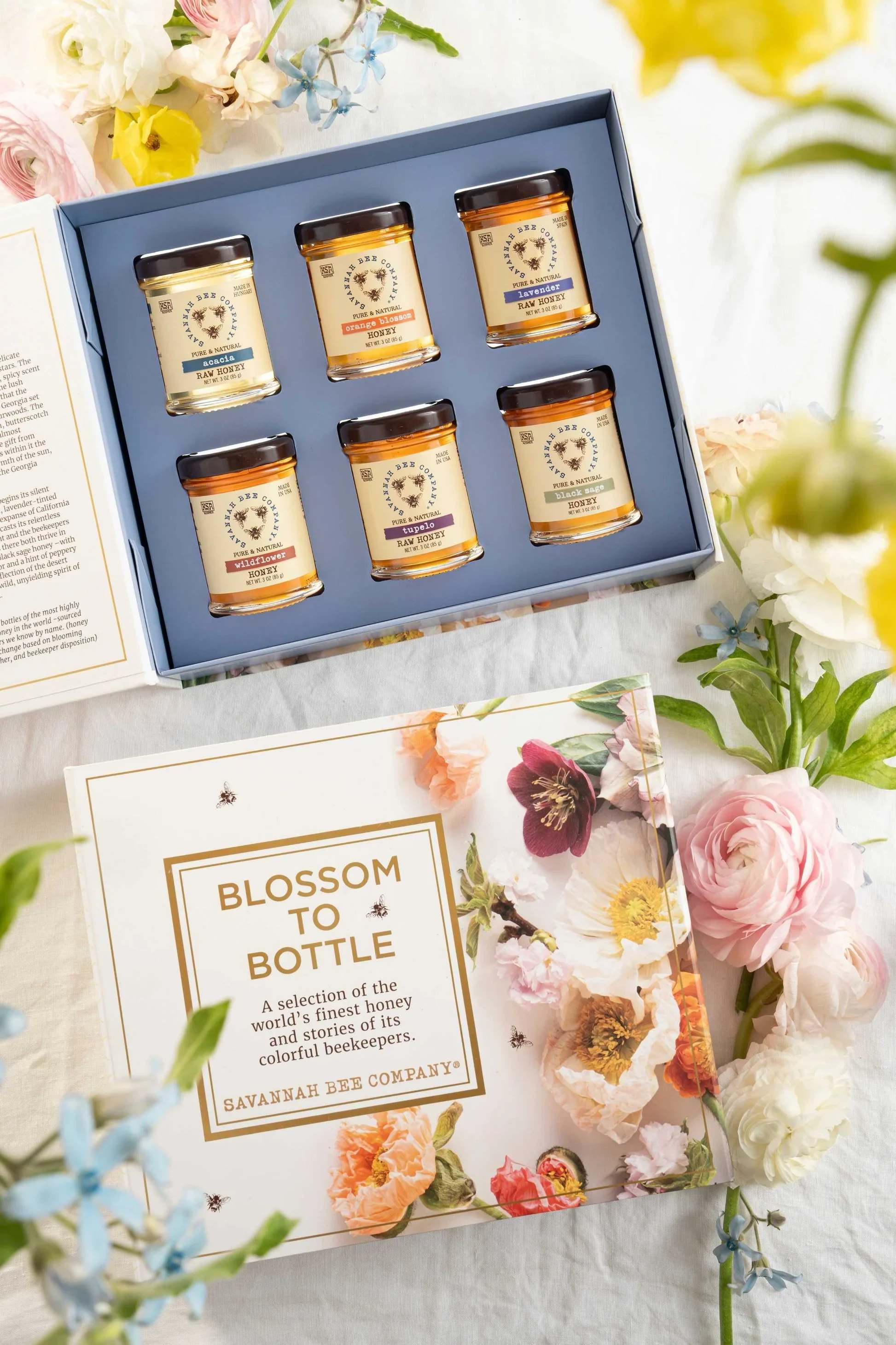Gift box with six honey jars beside floral packaging