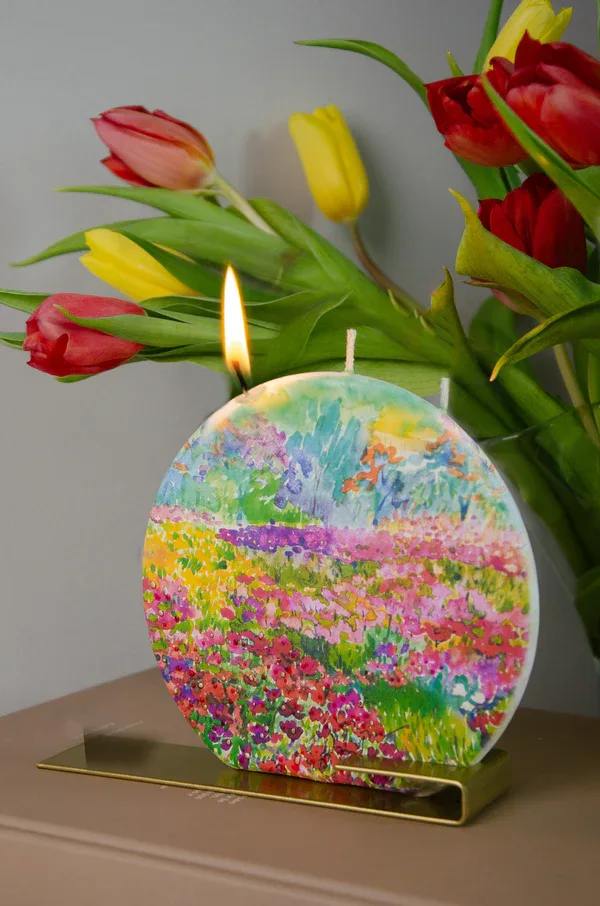 Tulips behind a colorful round candle with a lit wick