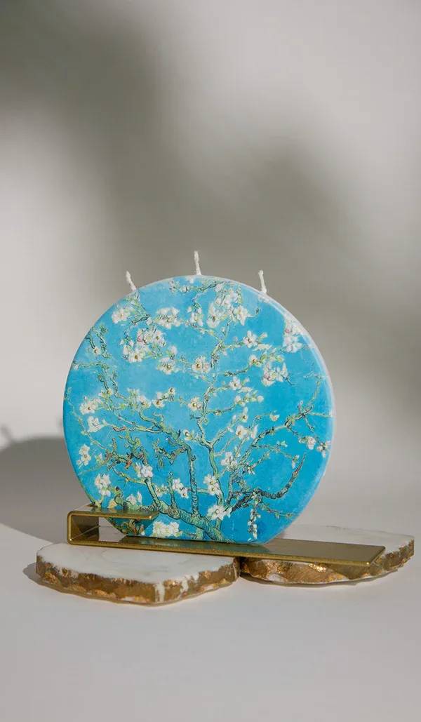 Round blue decorative candle with white blossoms on a gold stand