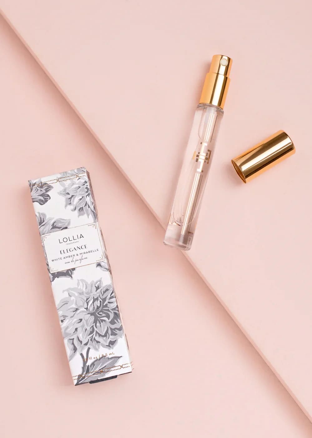 Perfume spray bottle with gold cap and matching box on a pink background