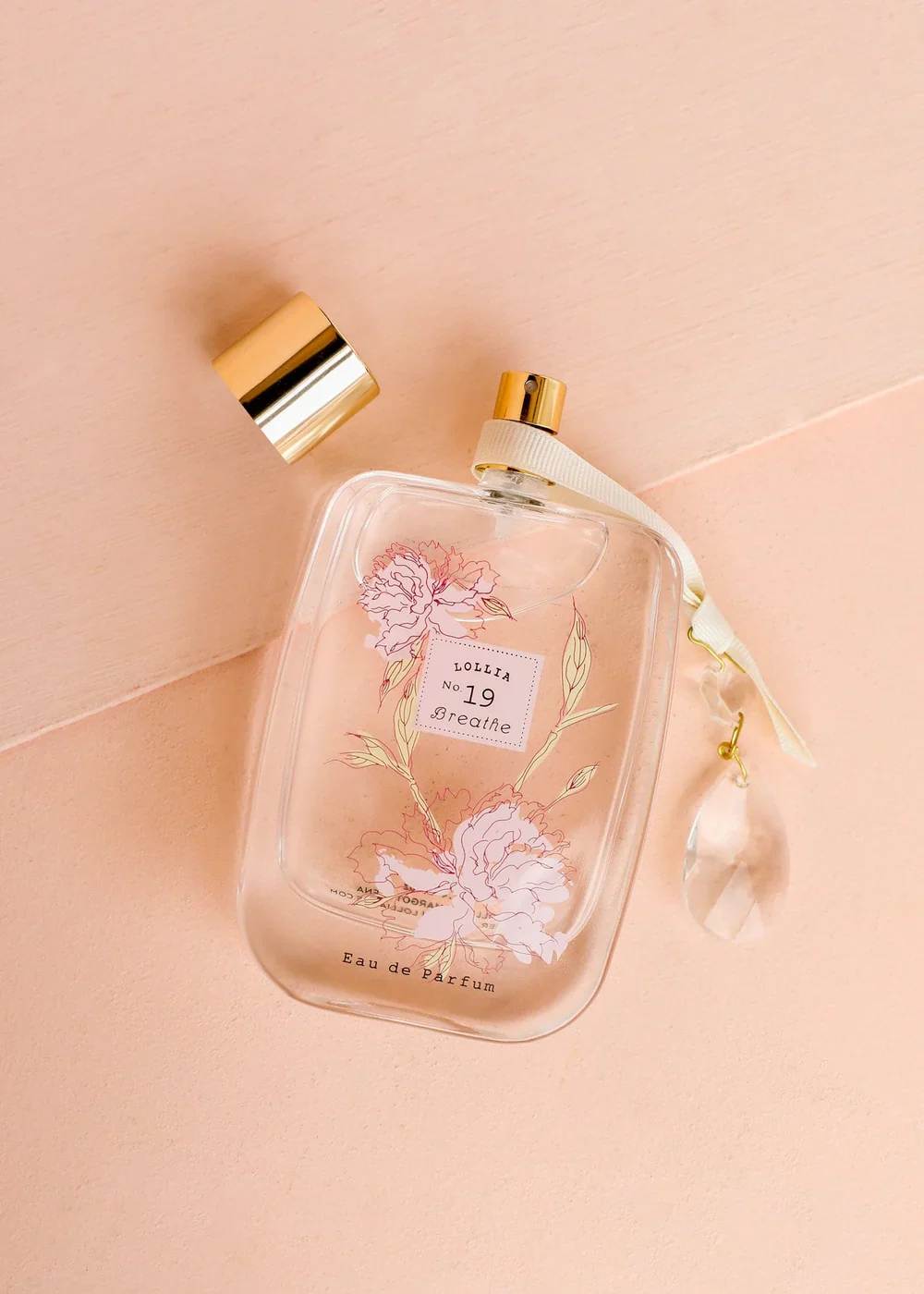 Clear perfume bottle with floral print and gold cap on a pink background