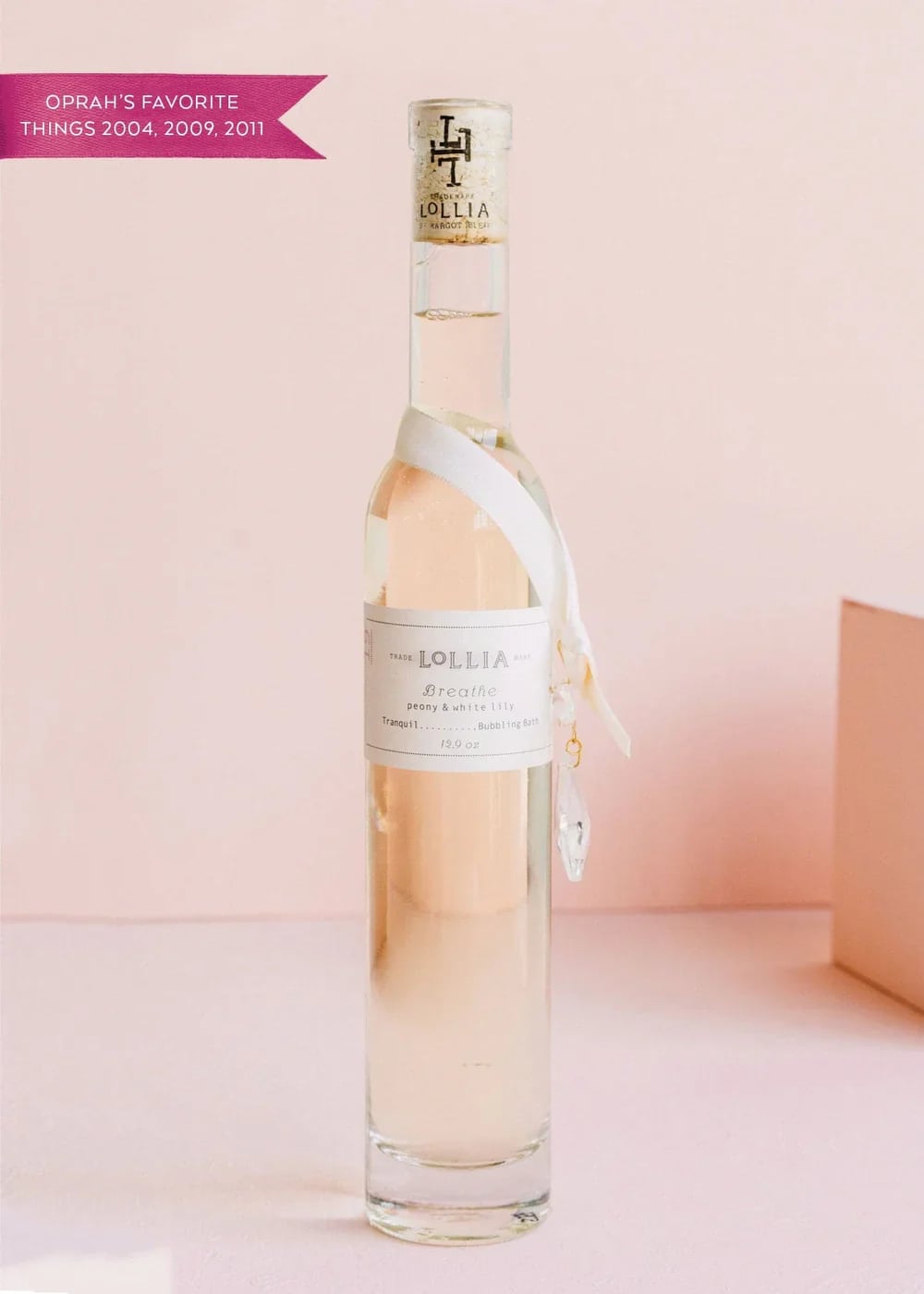 A tall clear bottle of Lollia bath oil with a ribbon tag