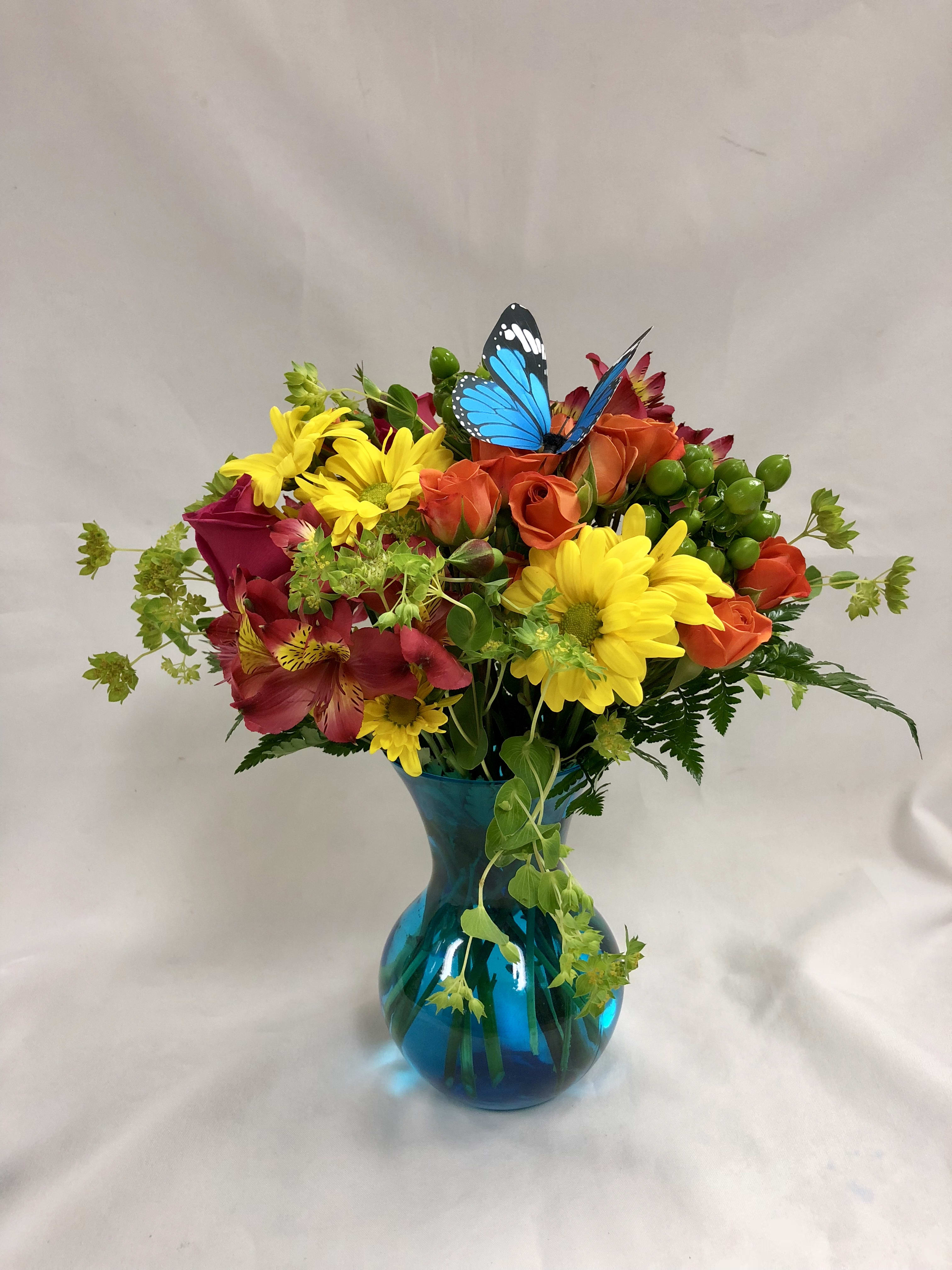 Butterfly Kisses - This arrangement is sure to brighten anyone's day!  Hot pink roses, orange spray roses, pink alstroemeria, yellow daisies, hypericum, bupleurum with a beautiful butterfly.  Deluxe version shown. Flowers and colors may vary due to stock availability.