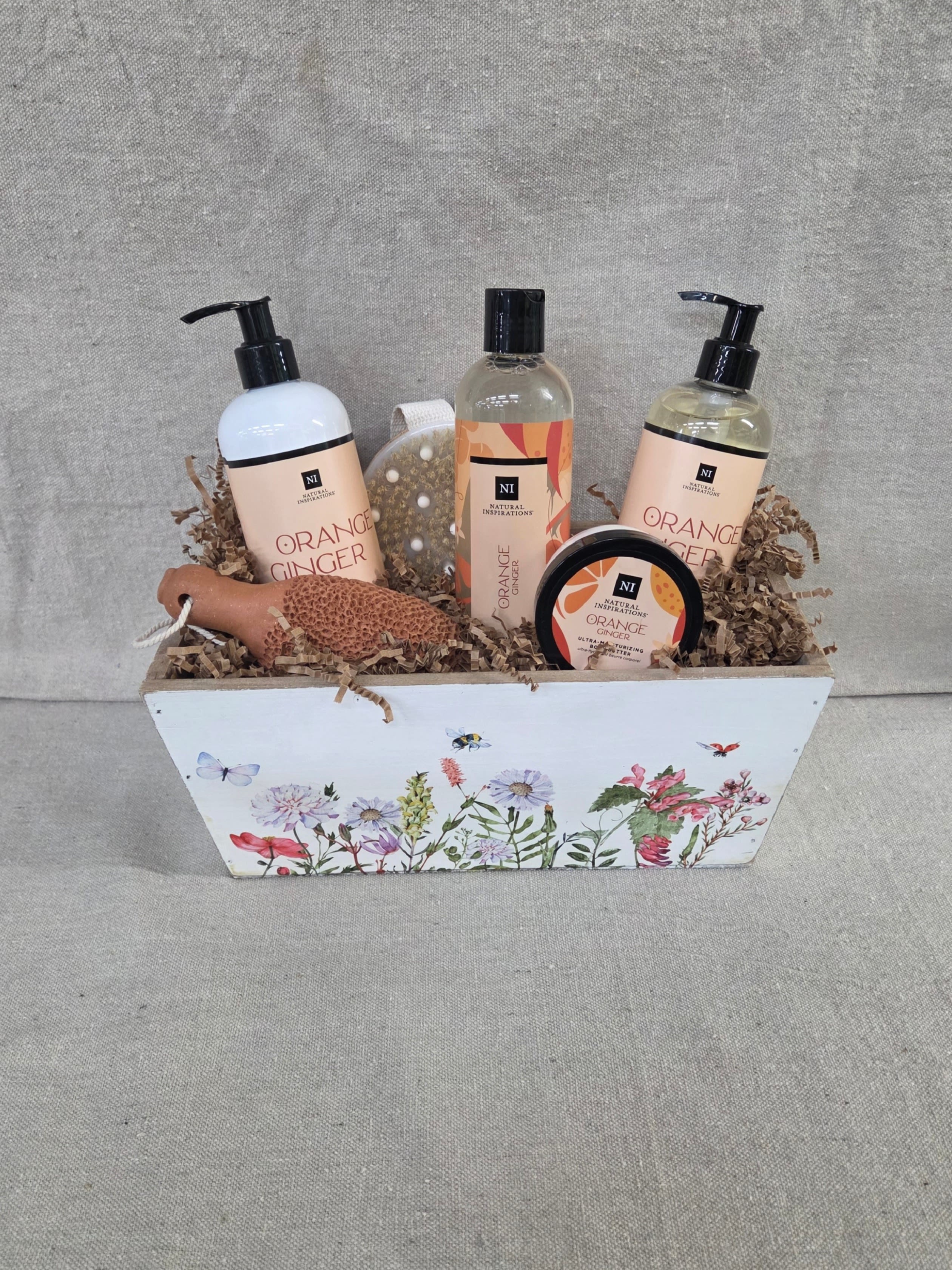 Bath gift set with orange ginger products in a floral-printed white wooden box filled with paper shred.