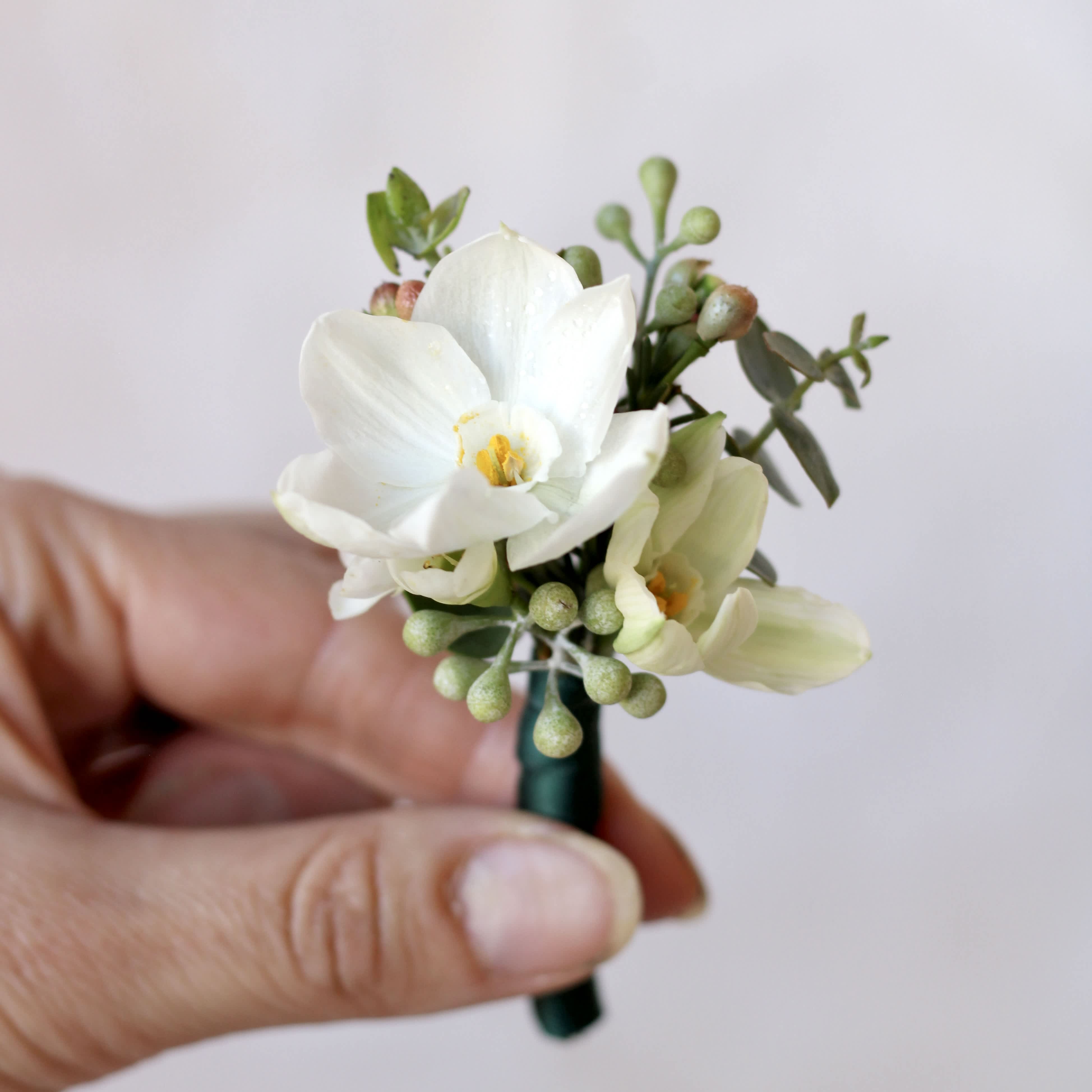 White boutonniere with small green accents held in a hand