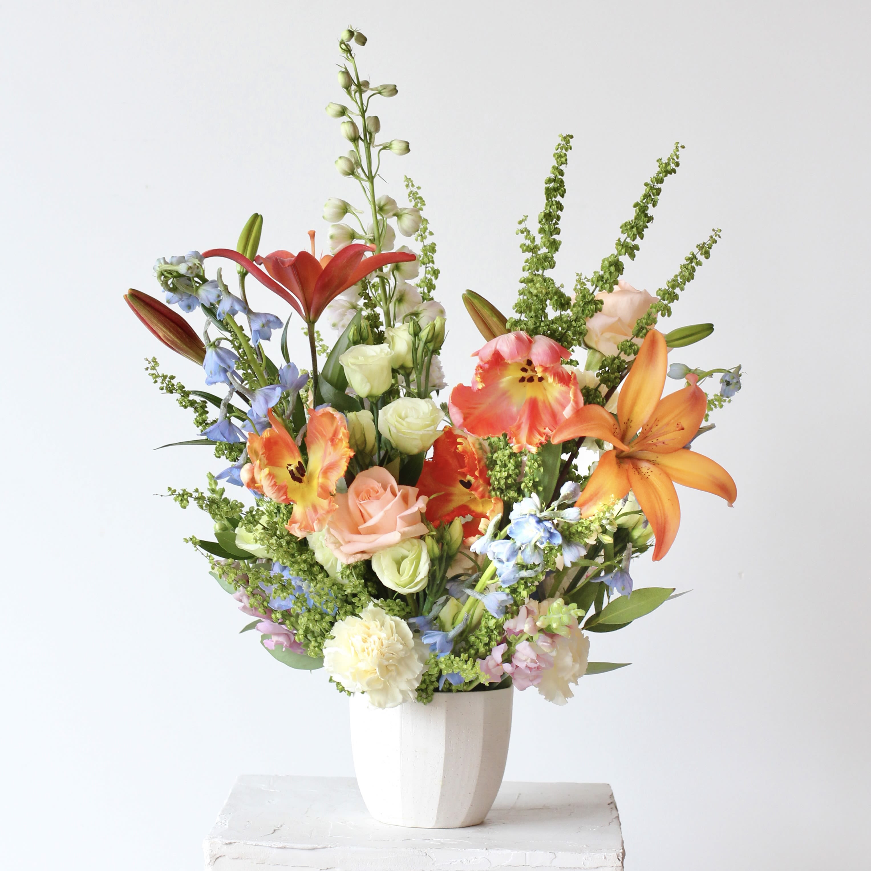 Mixed bouquet of lilies, roses, and blue flowers in a white vase