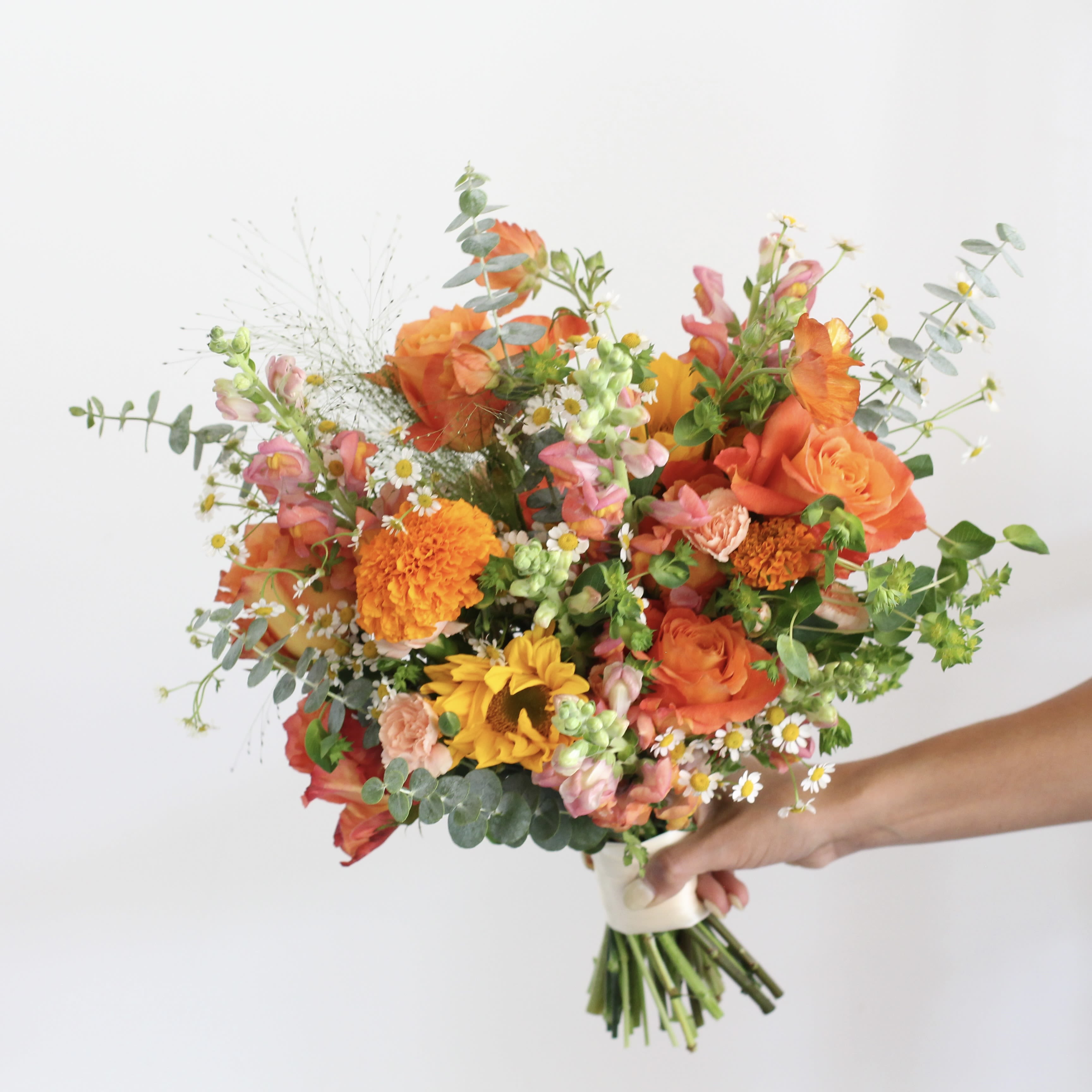 Handheld bouquet of orange, pink, and yellow flowers