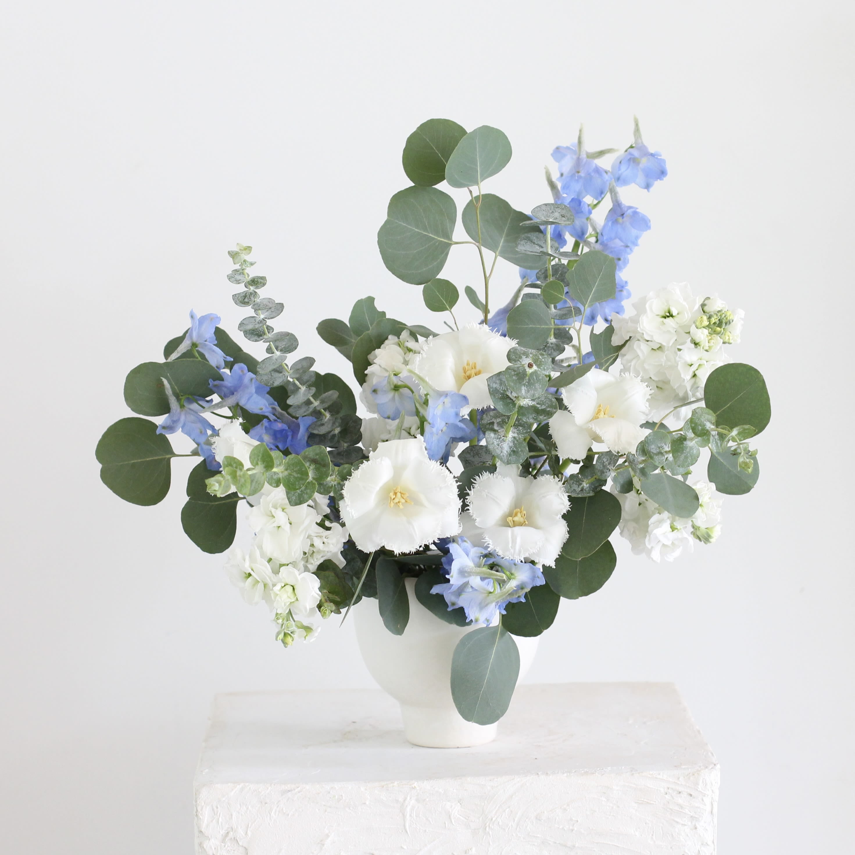 Blue and white flowers arranged in a white vase with round eucalyptus leaves
