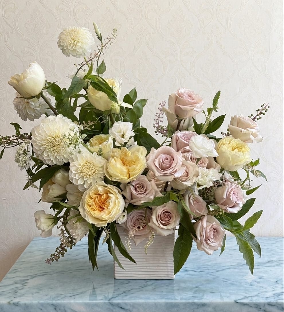 French Garden - This arrangement has an effortless elegance. Reminiscent of a French country garden in full bloom. The soft palette of blush, ivory, and buttery cream creates a feeling of quiet luxury, while the airy, organic design gives it the charm of flowers freshly gathered from the garden. A graceful composition of premium garden roses, delicate blush roses, lush peonies, elegant dahlias and seasonal blooms. 