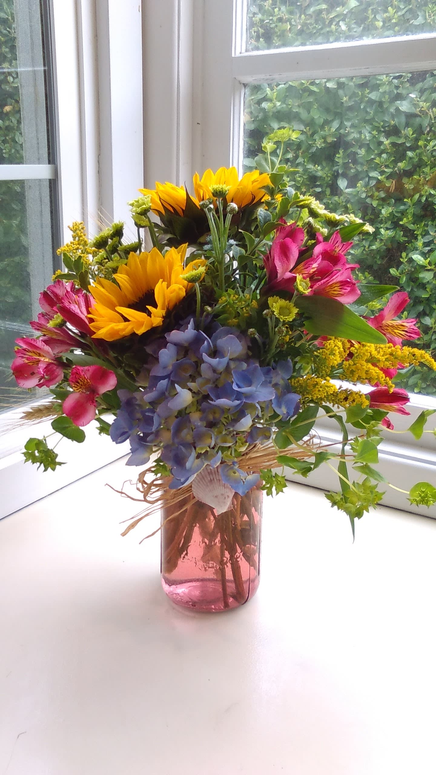 Mixed bouquet in a pink glass vase with sunflowers, pink alstroemeria, and blue hydrangea