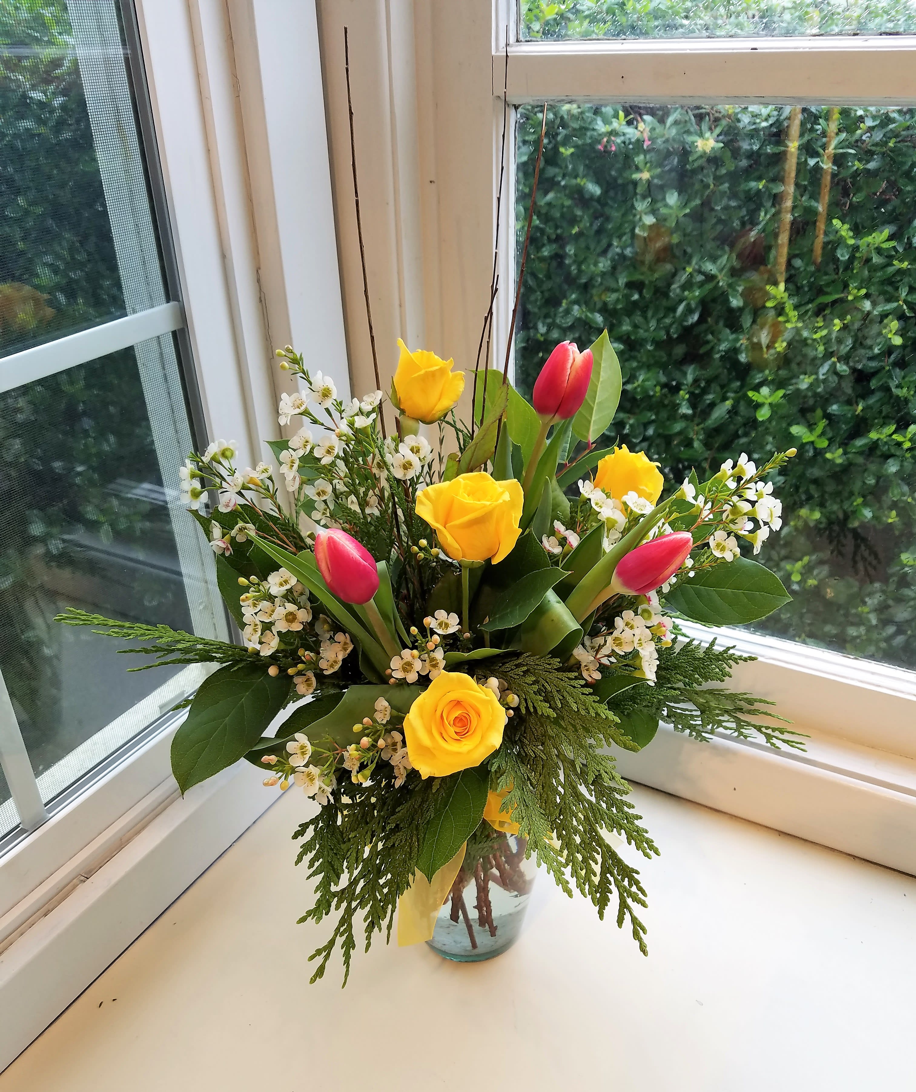Yellow roses and pink tulips in a glass vase with white filler flowers