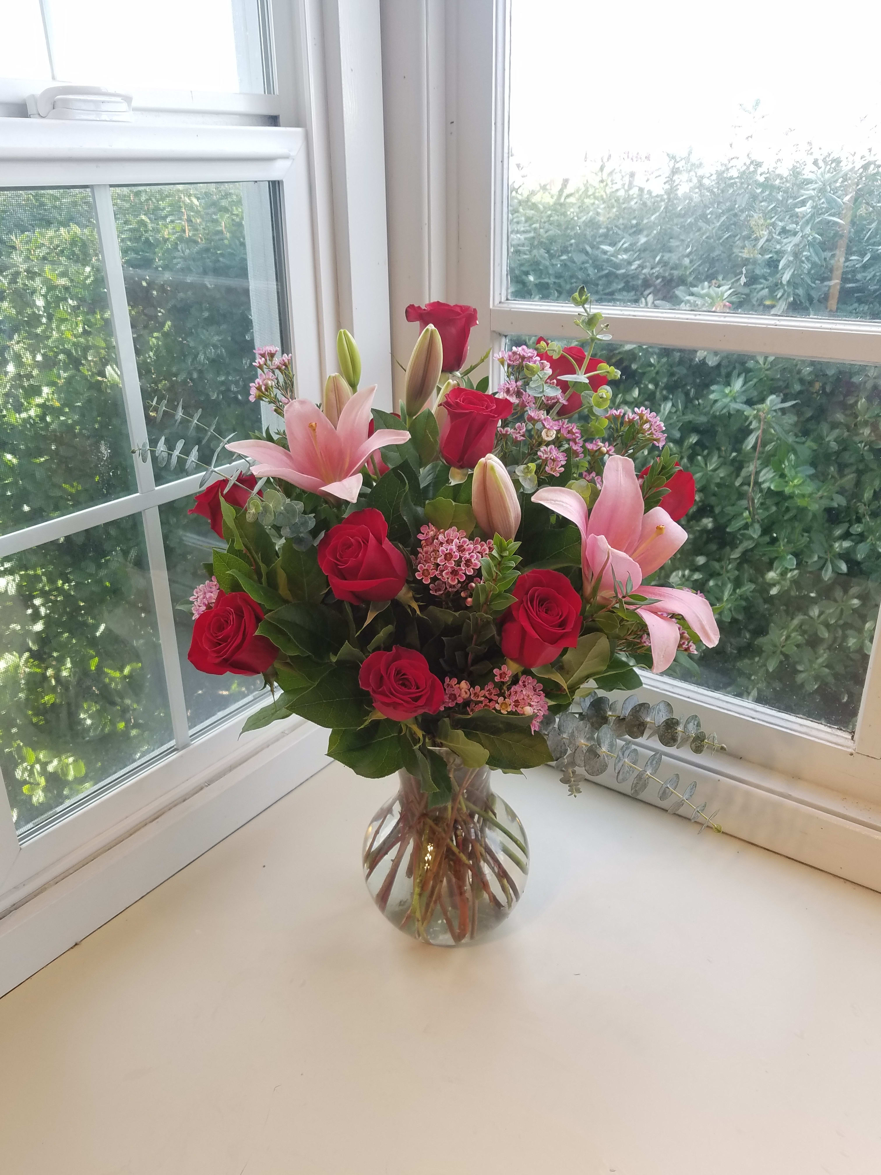 Pink lilies and red roses arranged in a clear glass vase