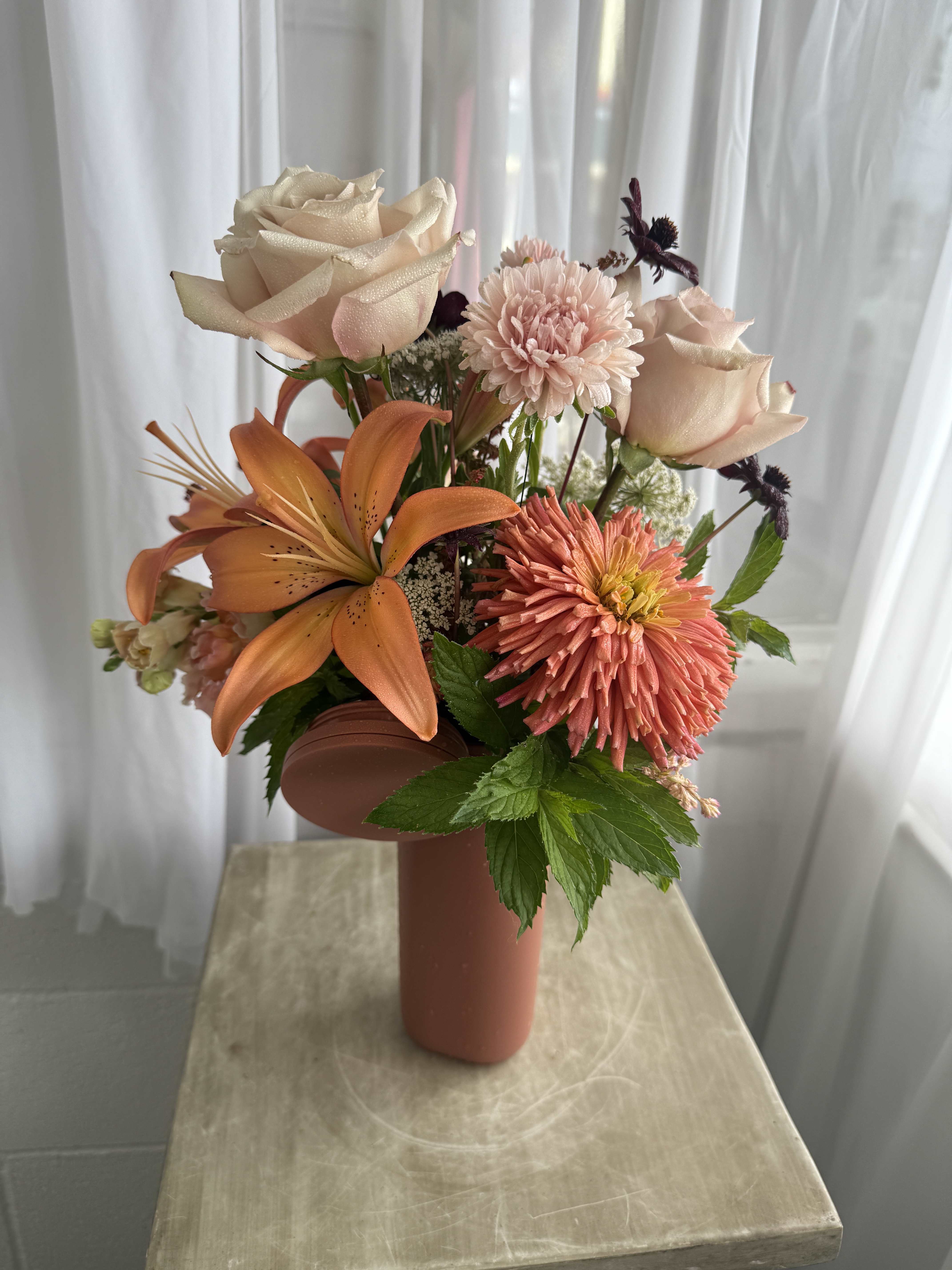Peach and cream floral arrangement in a tall vase with roses and lilies