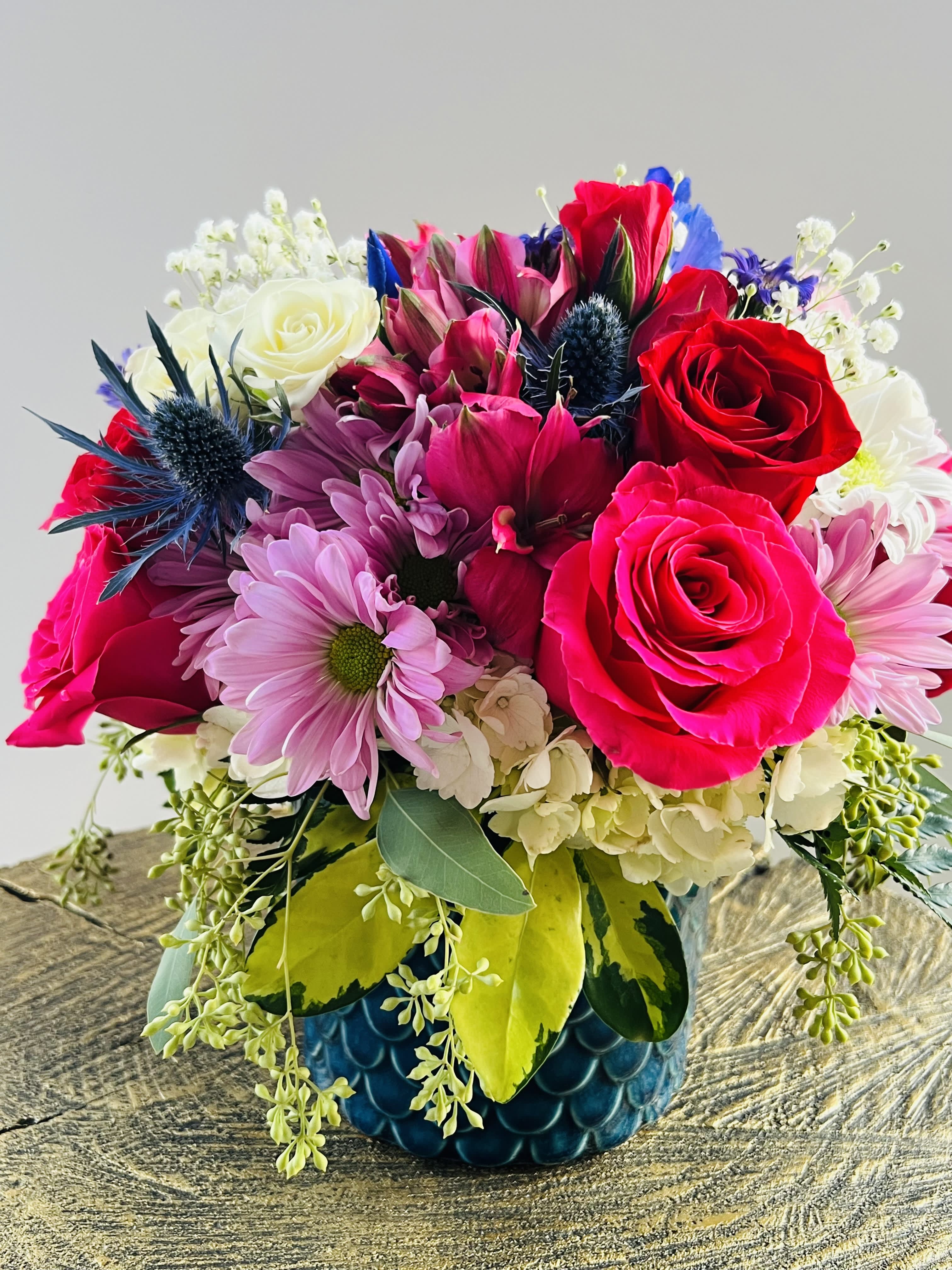 Mixed bouquet of red and pink roses with daisies in a blue vase