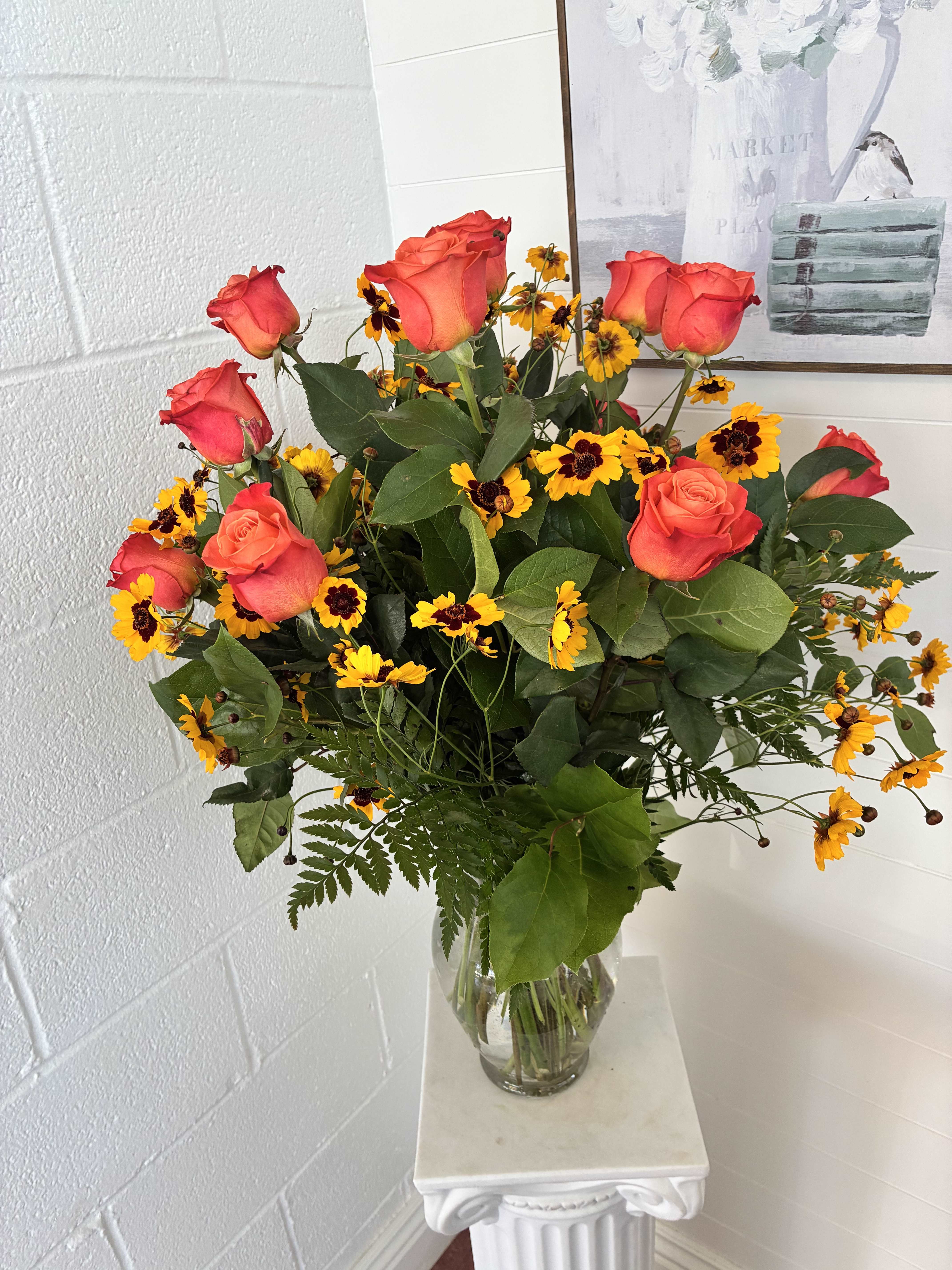 Bouquet of coral roses and yellow daisies in a clear glass vase